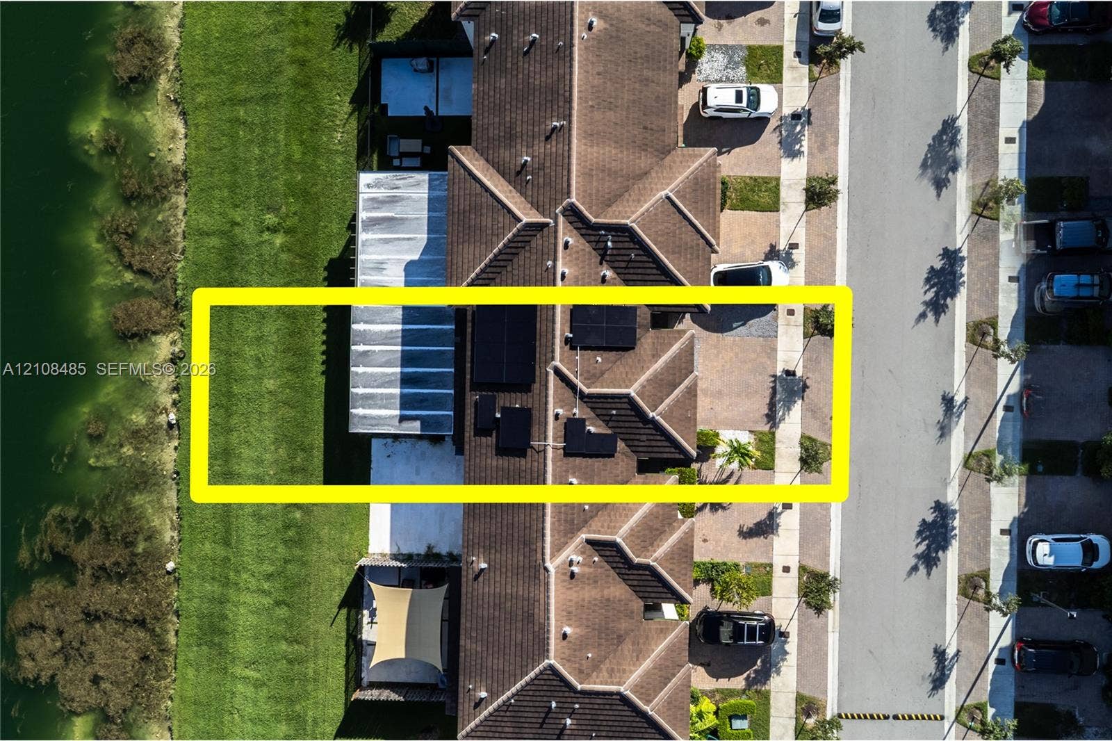 10217 SW 231st Lane, Miami, FL 33190 Aerial view featuring a tile roof, roof-mounted solar panels, paved driveway, and waterfront positioning