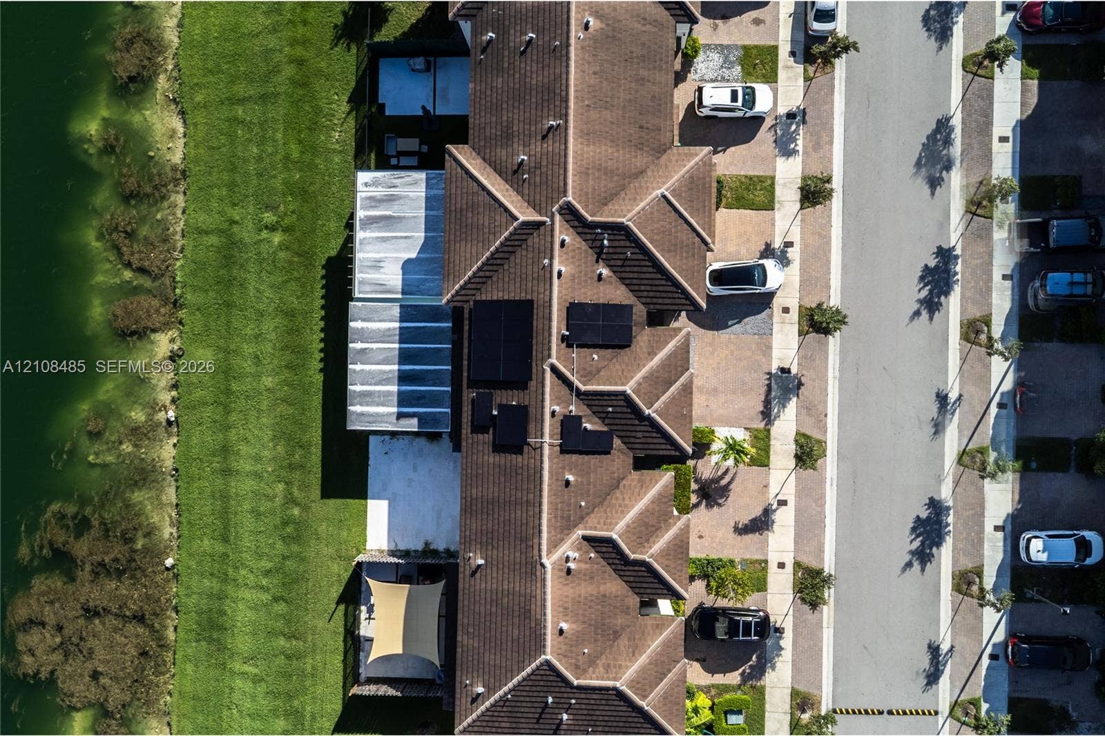 10217 SW 231st Lane, Miami, FL 33190 Aerial perspective of a multi-unit property featuring tiled roof lines, integrated solar energy panels, concrete hardscaping, and a grassed area bordering a water feature