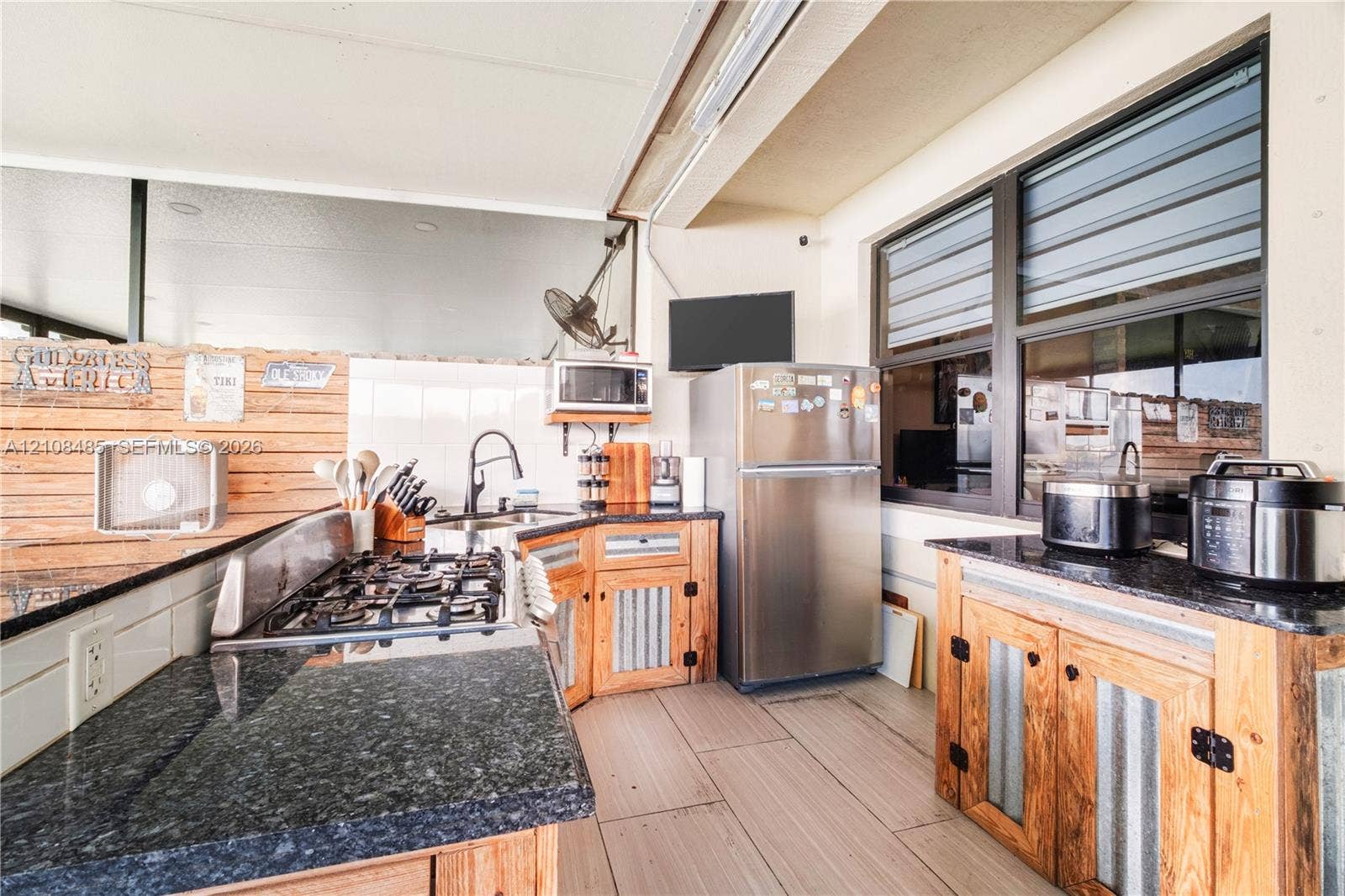 10217 SW 231st Lane, Miami, FL 33190 Outdoor kitchen featuring dark stone countertops, custom wood cabinetry with corrugated metal detailing, built-in stainless steel gas range, and large-format tile flooring