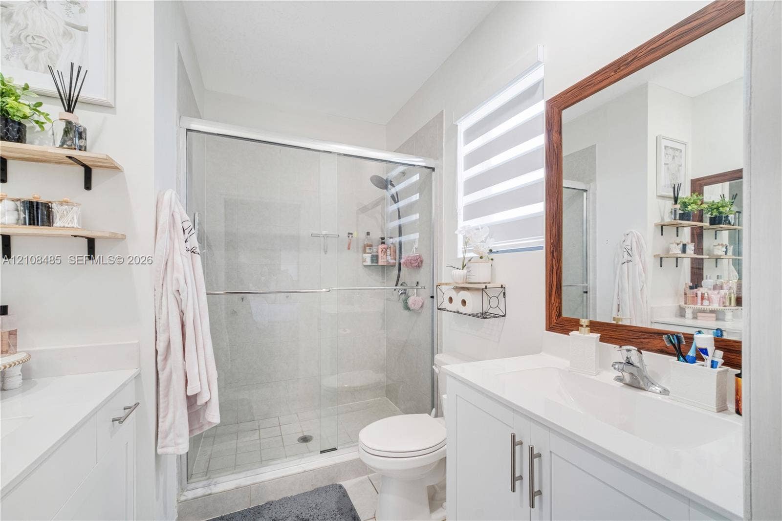 10217 SW 231st Lane, Miami, FL 33190 Bathroom featuring a vanity with a white countertop and rectangular undermount sink, a large wood-framed mirror, walk-in shower with glass enclosure, and wall-mounted shelving
