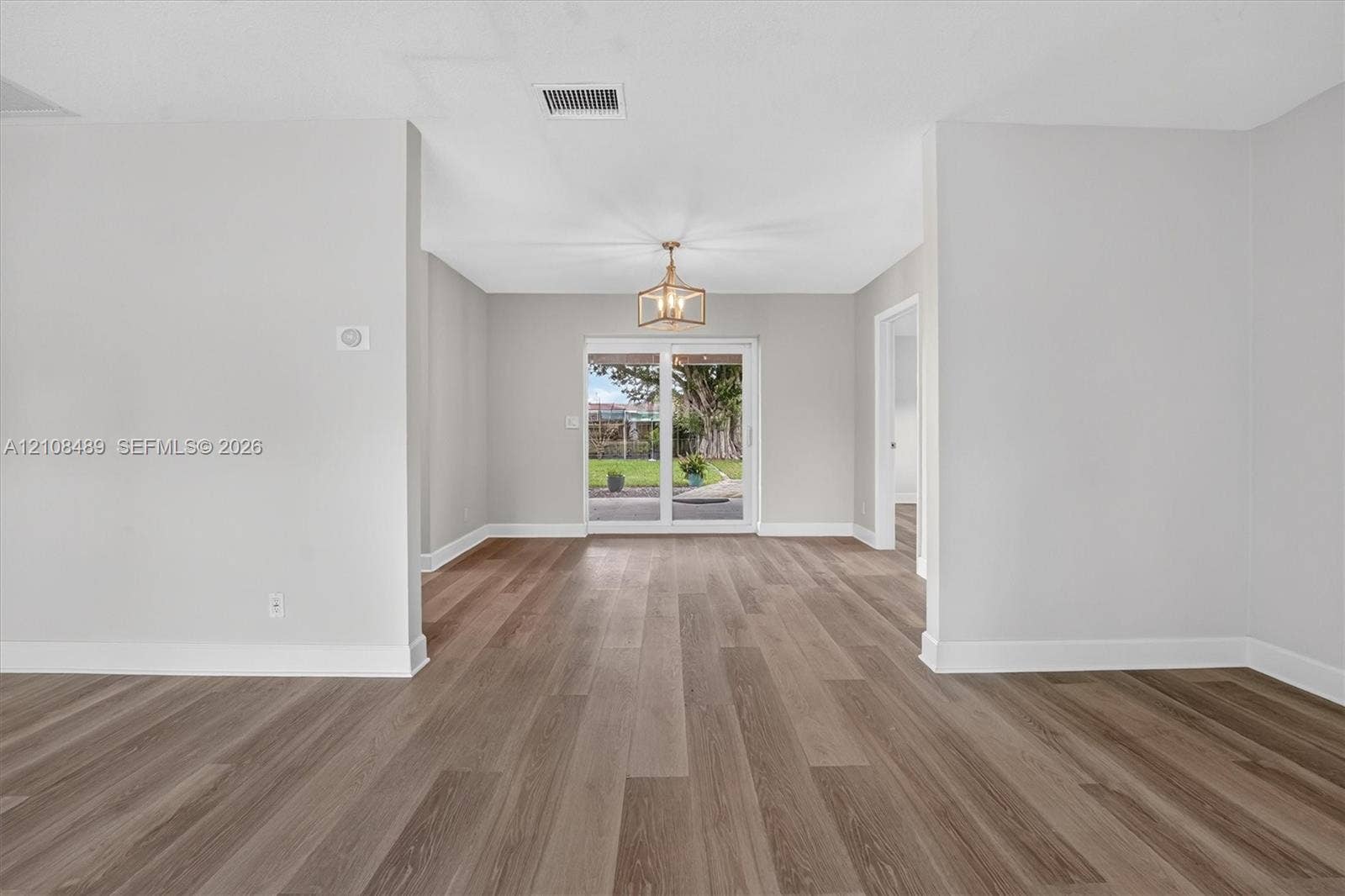 Interior space featuring wood-finish flooring, neutral wall tones, a geometric metal chandelier, and sliding glass doors