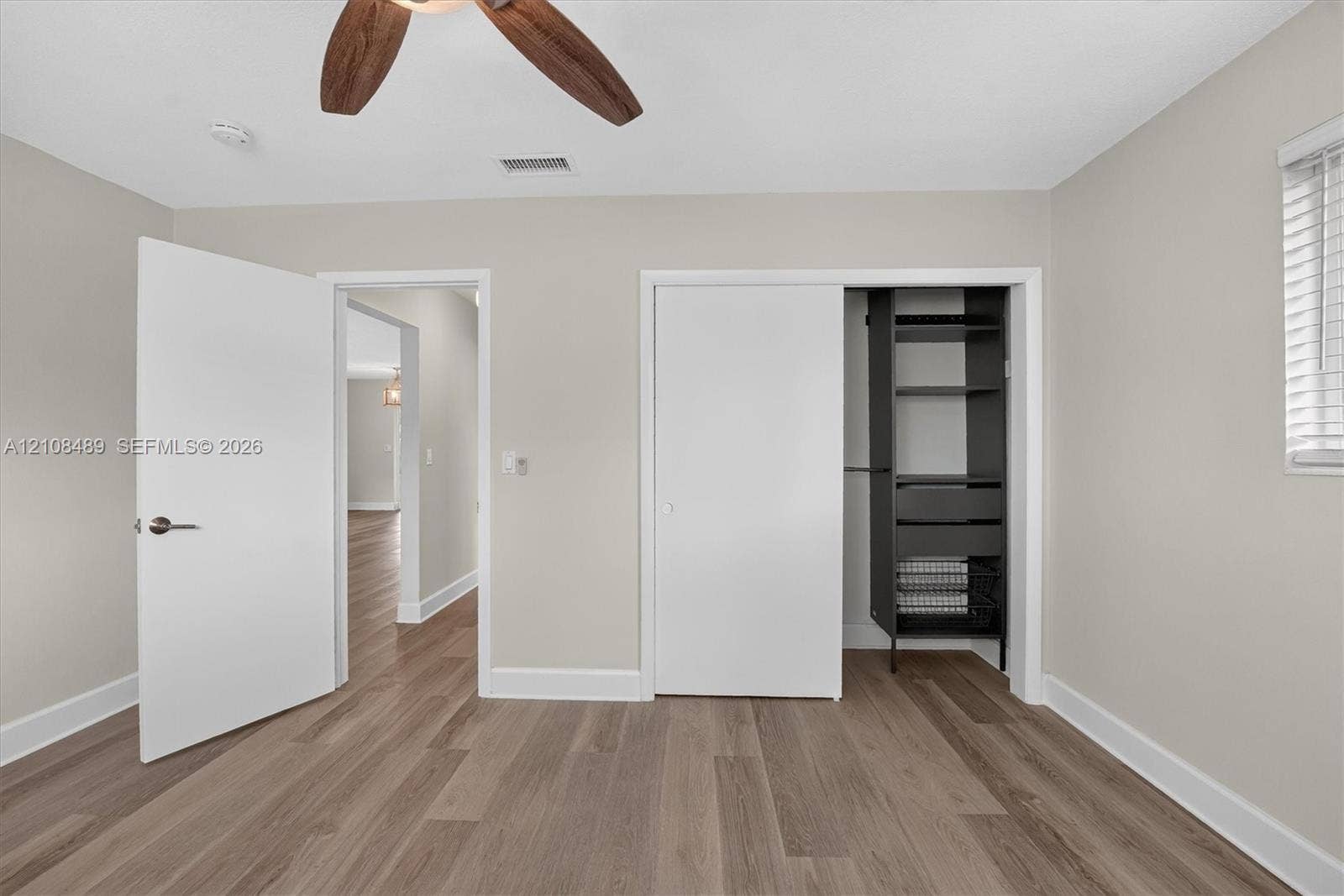 Wood-finish flooring, ceiling fan with wood-tone blades, built-in closet organization system, and white window blinds