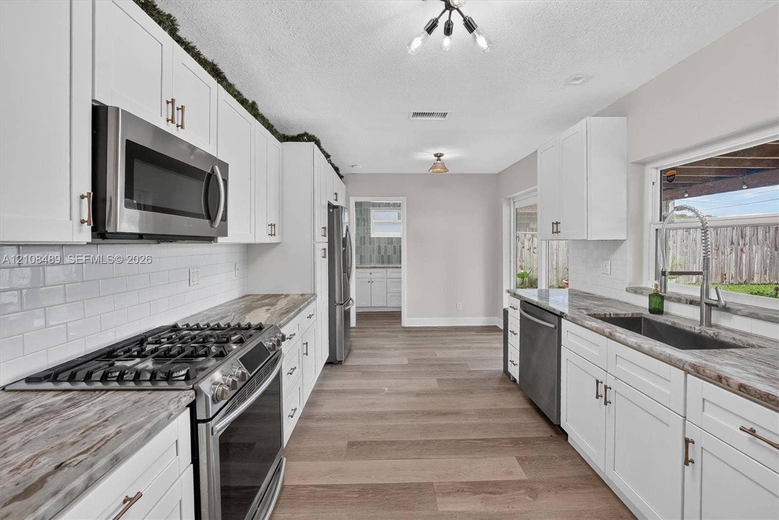 Kitchen featuring white shaker cabinetry, stone-patterned countertops, white subway tile backsplash, stainless steel appliances, and wood-finish flooring