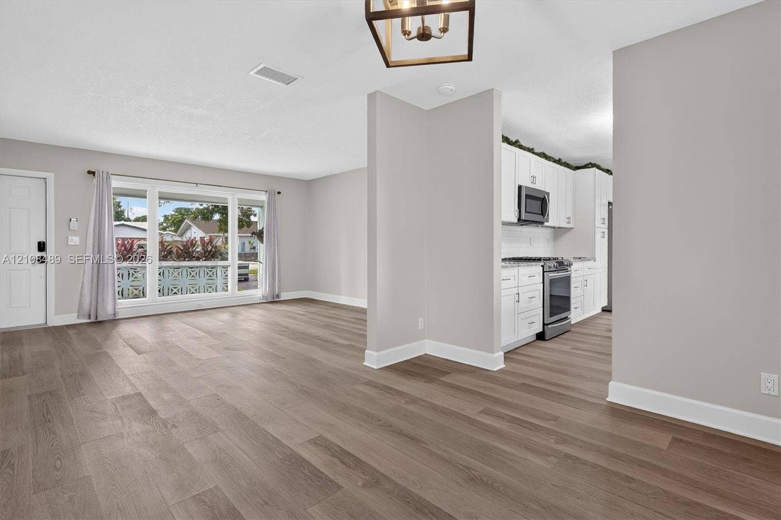 Open interior featuring wood-finish flooring, white cabinetry, integrated stainless steel appliances, a picture window, and a geometric pendant light fixture