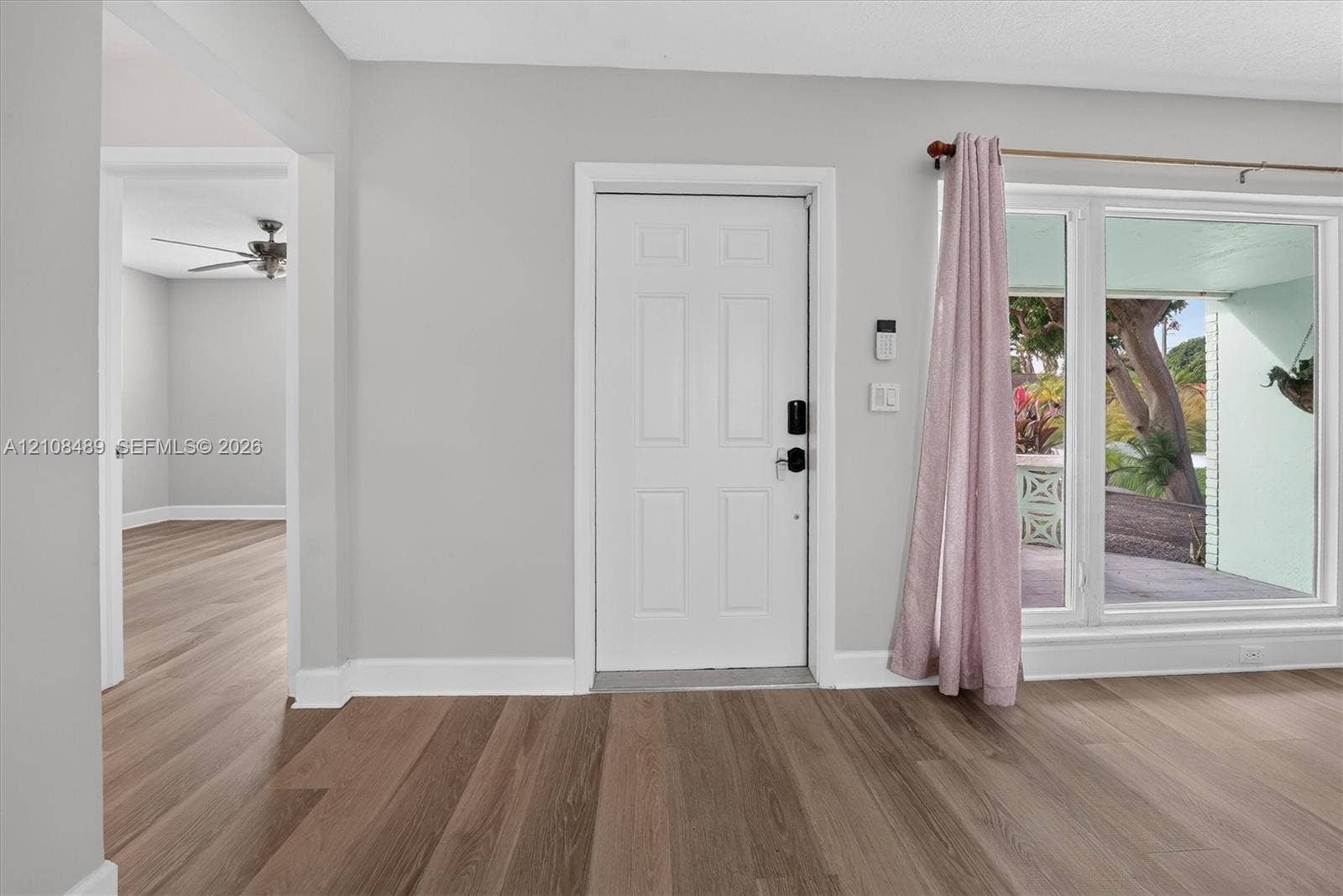 Neutral-toned interior featuring wood-finish flooring, a white six-panel entry door, and expansive glass window panes