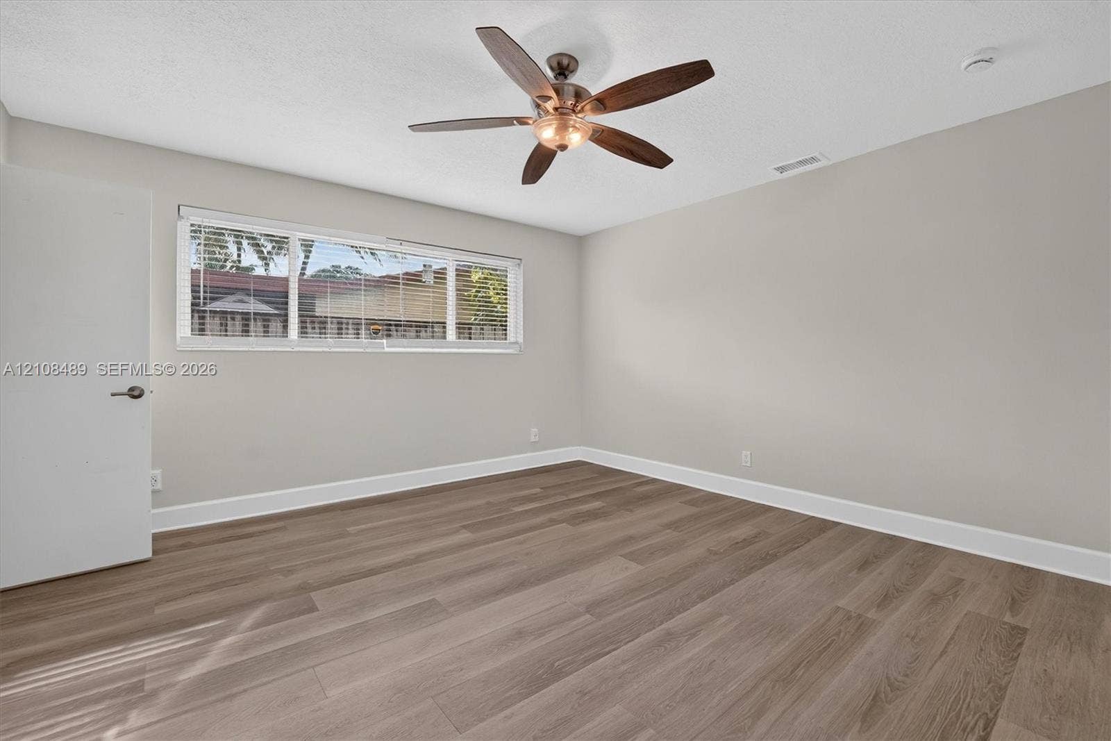 Room featuring wood-finish flooring, a multi-blade ceiling fan with integrated lighting, and a large horizontal window