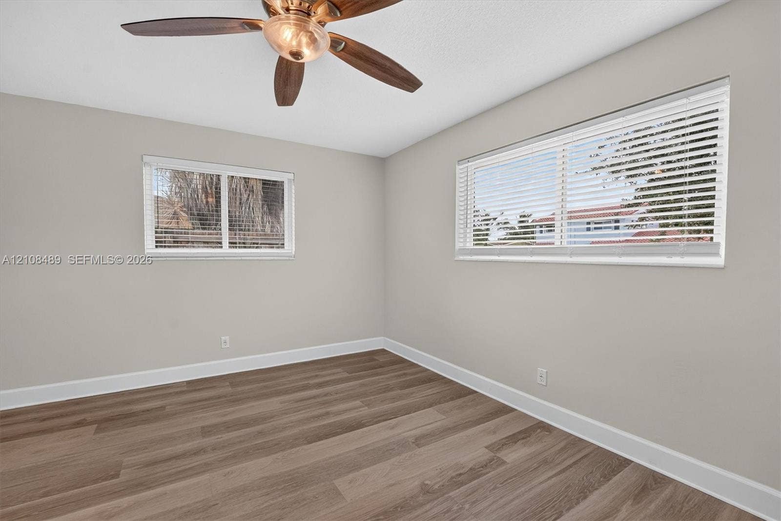 Interior space featuring wood-finish flooring, two dual-pane windows with horizontal blinds, and a multi-blade ceiling fan with integrated light fixture
