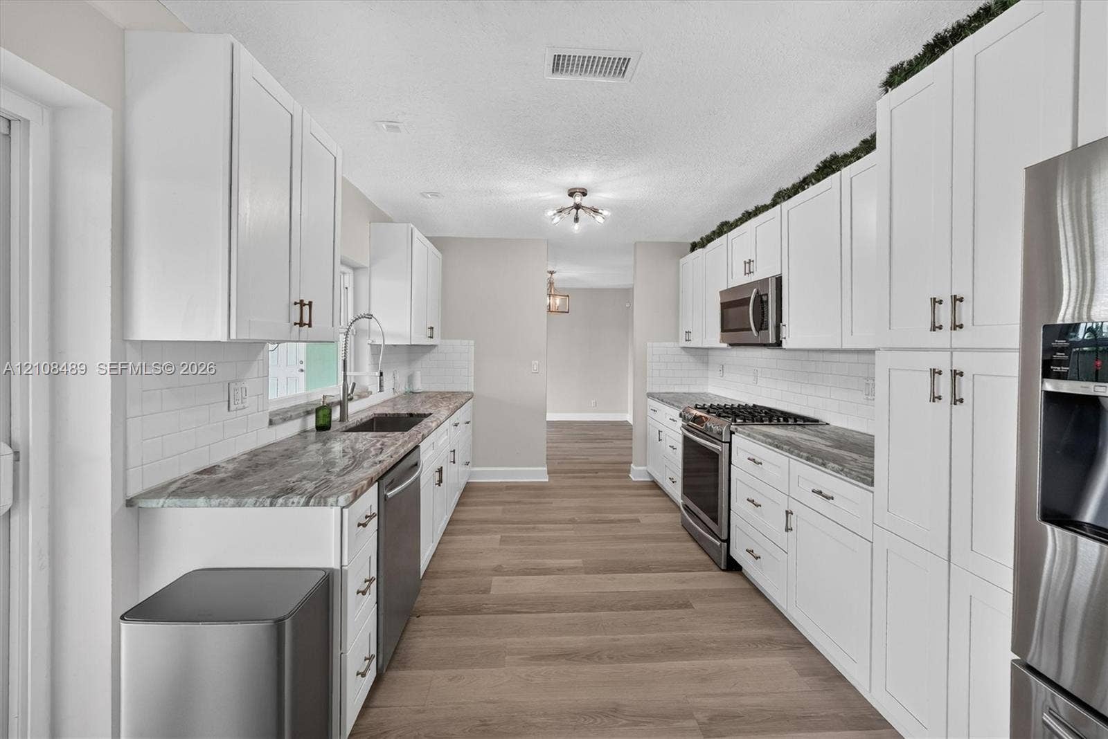 Kitchen featuring white shaker-style cabinetry, stone-patterned countertops, white subway tile backsplash, stainless steel appliances, and wood-finish flooring