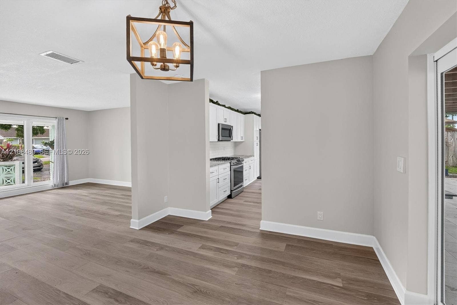Wood-finish flooring throughout, kitchen featuring white cabinetry and stainless steel appliances, and a geometric metal chandelier
