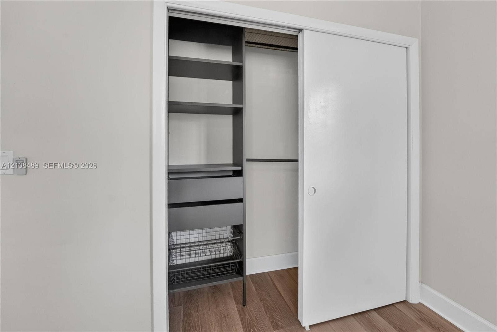 Reach-in closet featuring custom organizational cabinetry, including integrated shelving, dual storage drawers, and metal wire pull-out baskets, complemented by wood-finish flooring