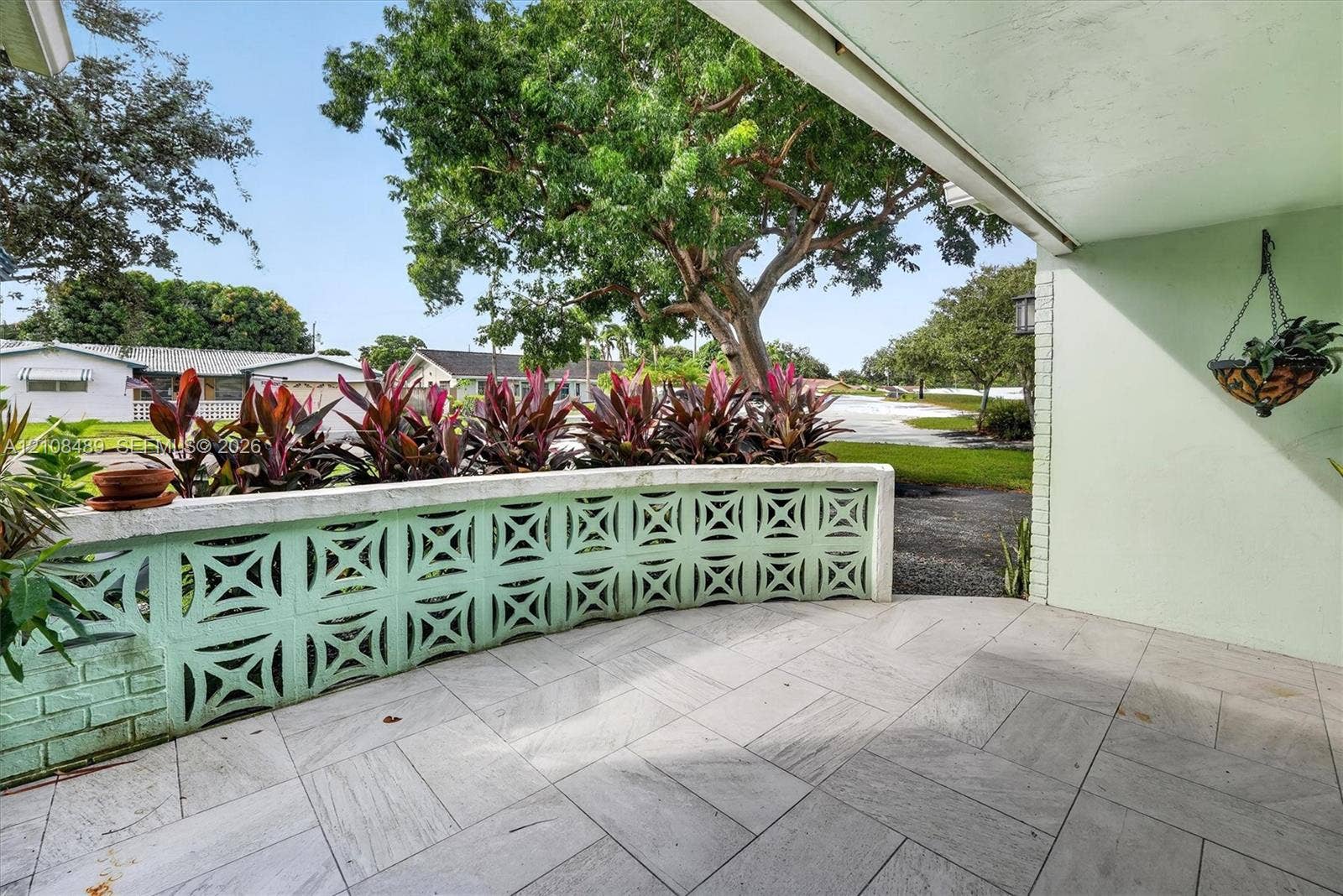 Covered patio featuring large-format stone-style tile flooring and a decorative breeze block privacy wall topped with established tropical foliage