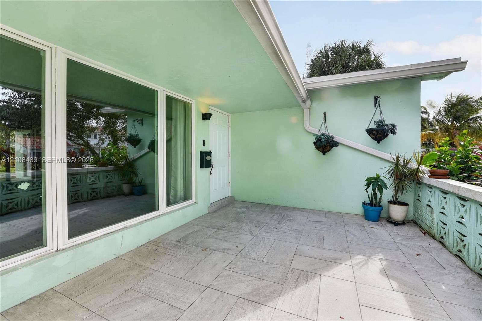 Covered entryway featuring large-format stone-tile flooring, expansive picture windows, and decorative concrete screen block accents
