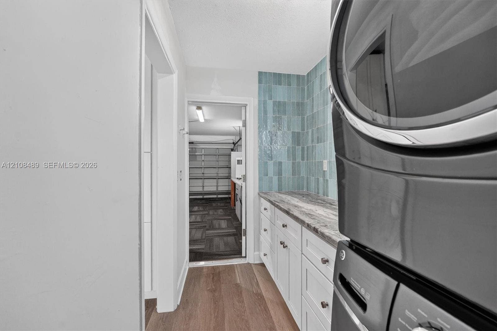 Utility room featuring white shaker-style cabinetry, stone-finish countertops, blue vertical tile backsplash, and wood-finish flooring