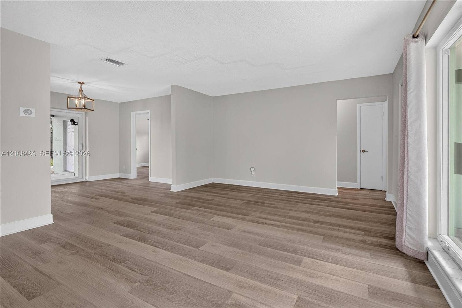 Neutral interior featuring wood-finish flooring, light gray walls, a geometric metal chandelier, and a sliding glass door