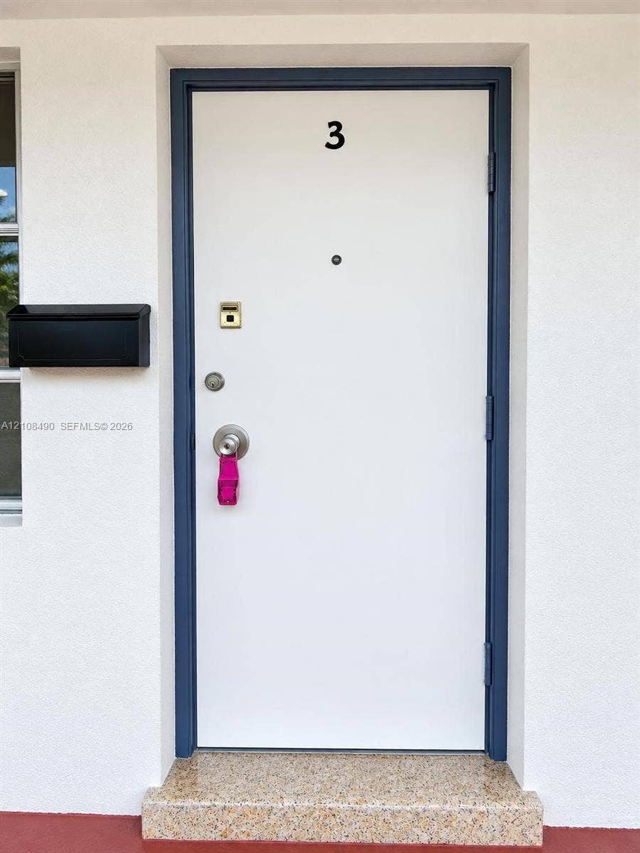 Entry featuring a white door with a dark blue frame, matte black wall-mounted mailbox, and stone-finish threshold
