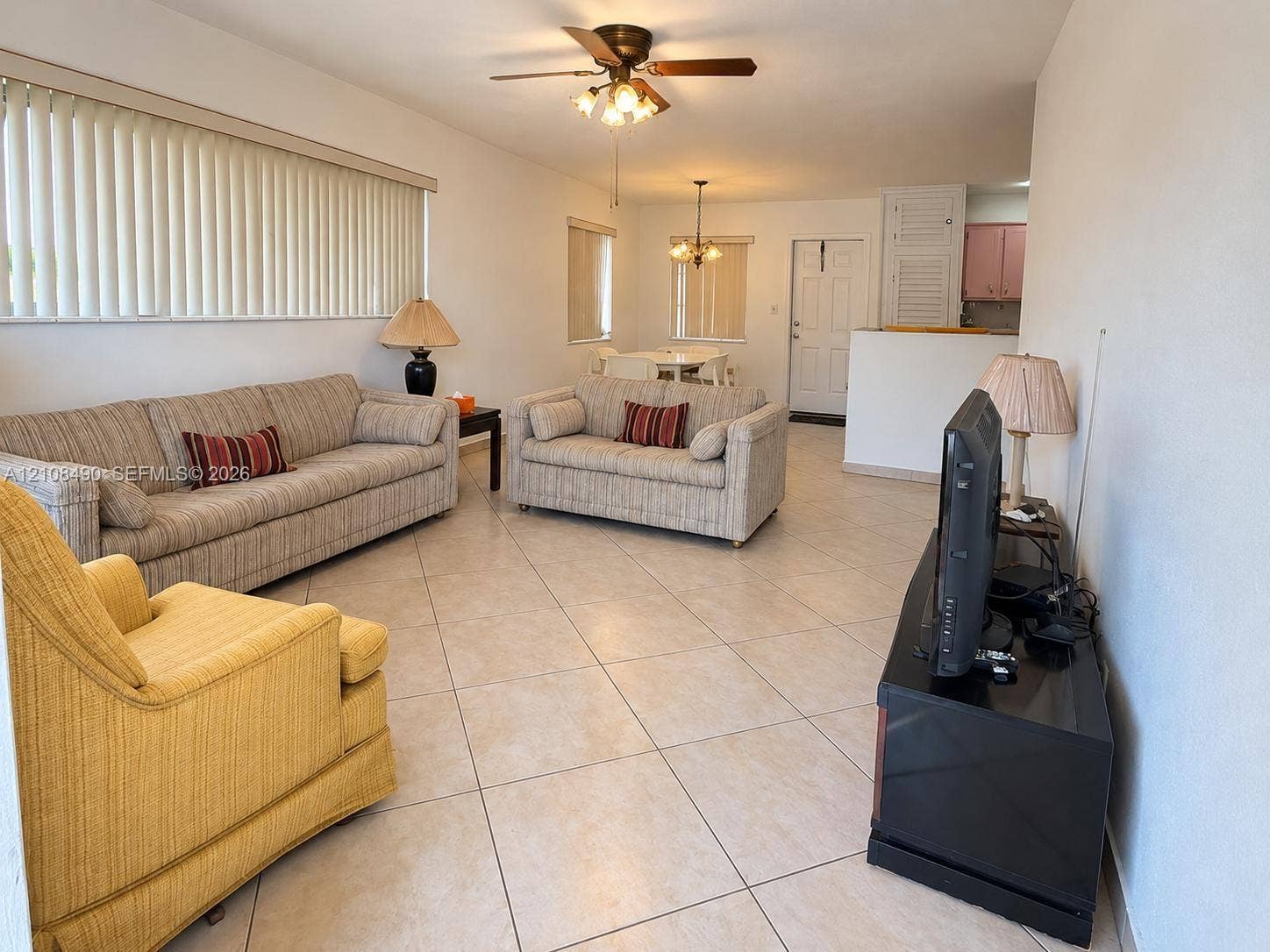 Neutral tile flooring, ceiling fan with light fixture, decorative multi-light chandelier, and horizontal window blinds