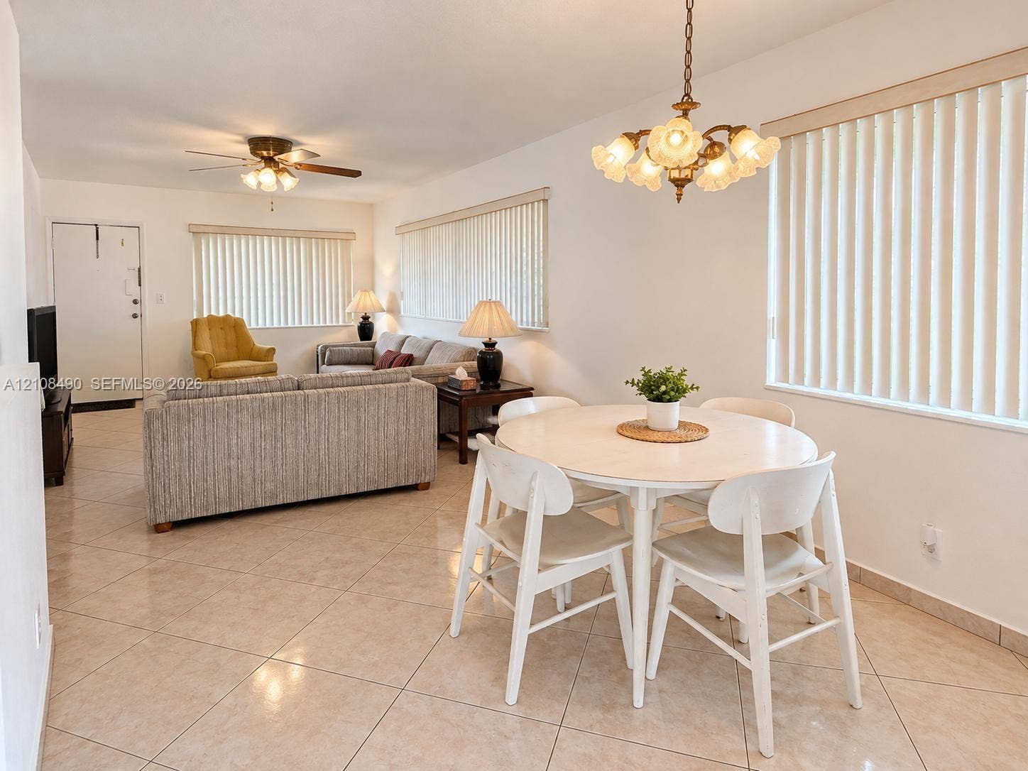 Large-format tile flooring, multi-arm decorative chandelier, ceiling fan with light fixture, and vertical window blinds