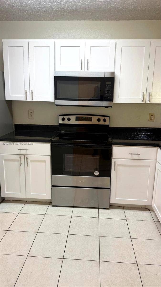 11233 W Atlantic Boulevard, #103, Coral Springs, Coral Springs, FL 33071 Kitchen featuring white shaker-style cabinetry, dark stone-finish countertops, stainless steel appliances, and large-format ceramic tile flooring