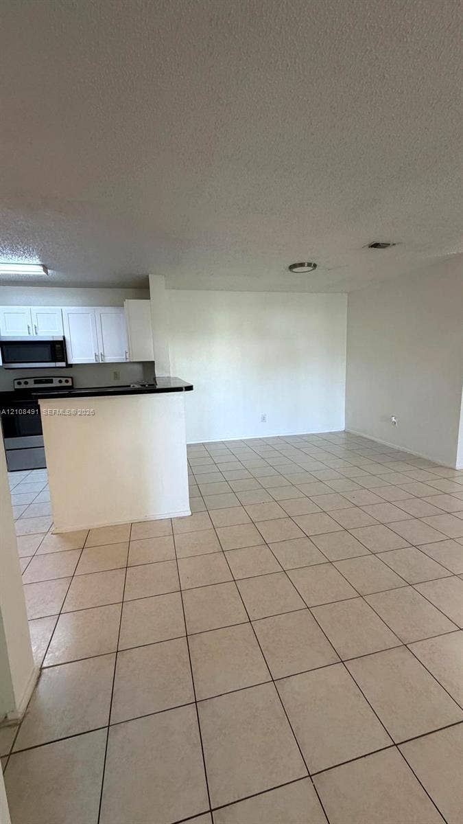 11233 W Atlantic Boulevard, #103, Coral Springs, Coral Springs, FL 33071 Open-concept interior featuring light-toned tile flooring, recessed ceiling lighting, and a kitchen peninsula with a dark countertop
