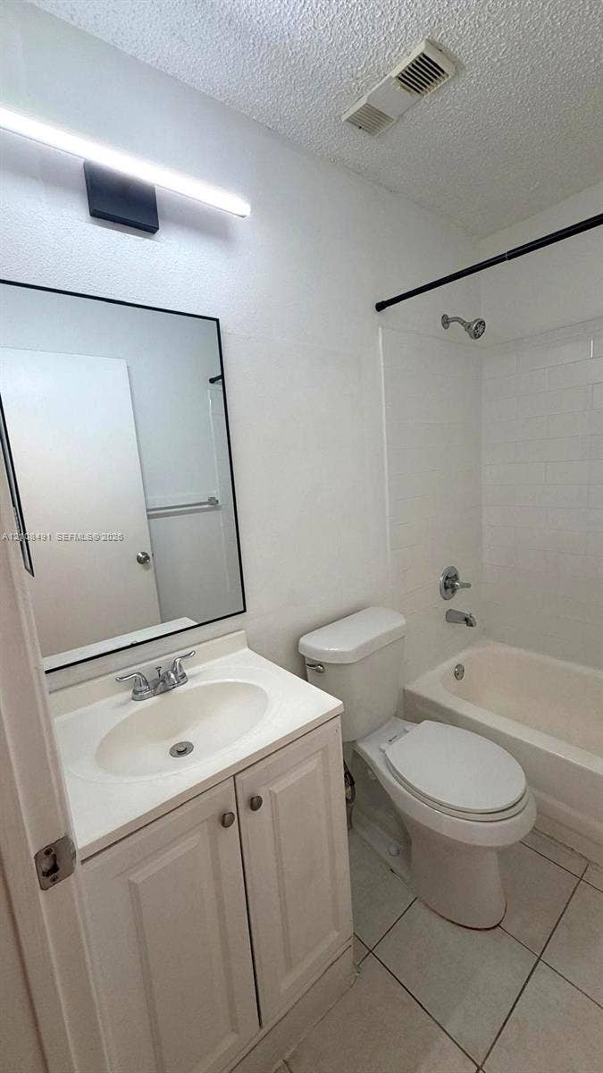 11233 W Atlantic Boulevard, #103, Coral Springs, Coral Springs, FL 33071 Bathroom featuring a vanity with a white integrated countertop, wall-mounted light fixture, rectangular mirror with a black frame, tile flooring, and a tub-shower combination with tile surround