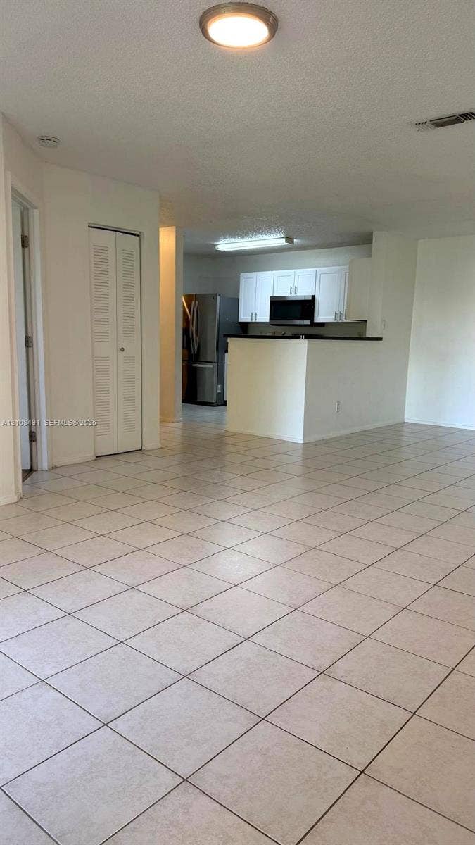 11233 W Atlantic Boulevard, #103, Coral Springs, Coral Springs, FL 33071 Open-concept interior featuring neutral tile flooring, white cabinetry, integrated stainless steel appliances, and a breakfast bar