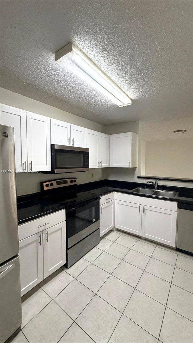 11233 W Atlantic Boulevard, #103, Coral Springs, Coral Springs, FL 33071 White shaker-style cabinetry, dark solid-surface countertops, stainless steel appliances, dual-basin stainless steel sink, and ceramic tile flooring