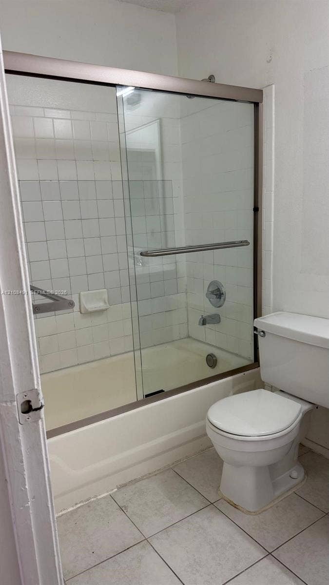 11233 W Atlantic Boulevard, #103, Coral Springs, Coral Springs, FL 33071 Bathtub with sliding glass enclosure, white tile surround, integrated soap dish, and porcelain toilet