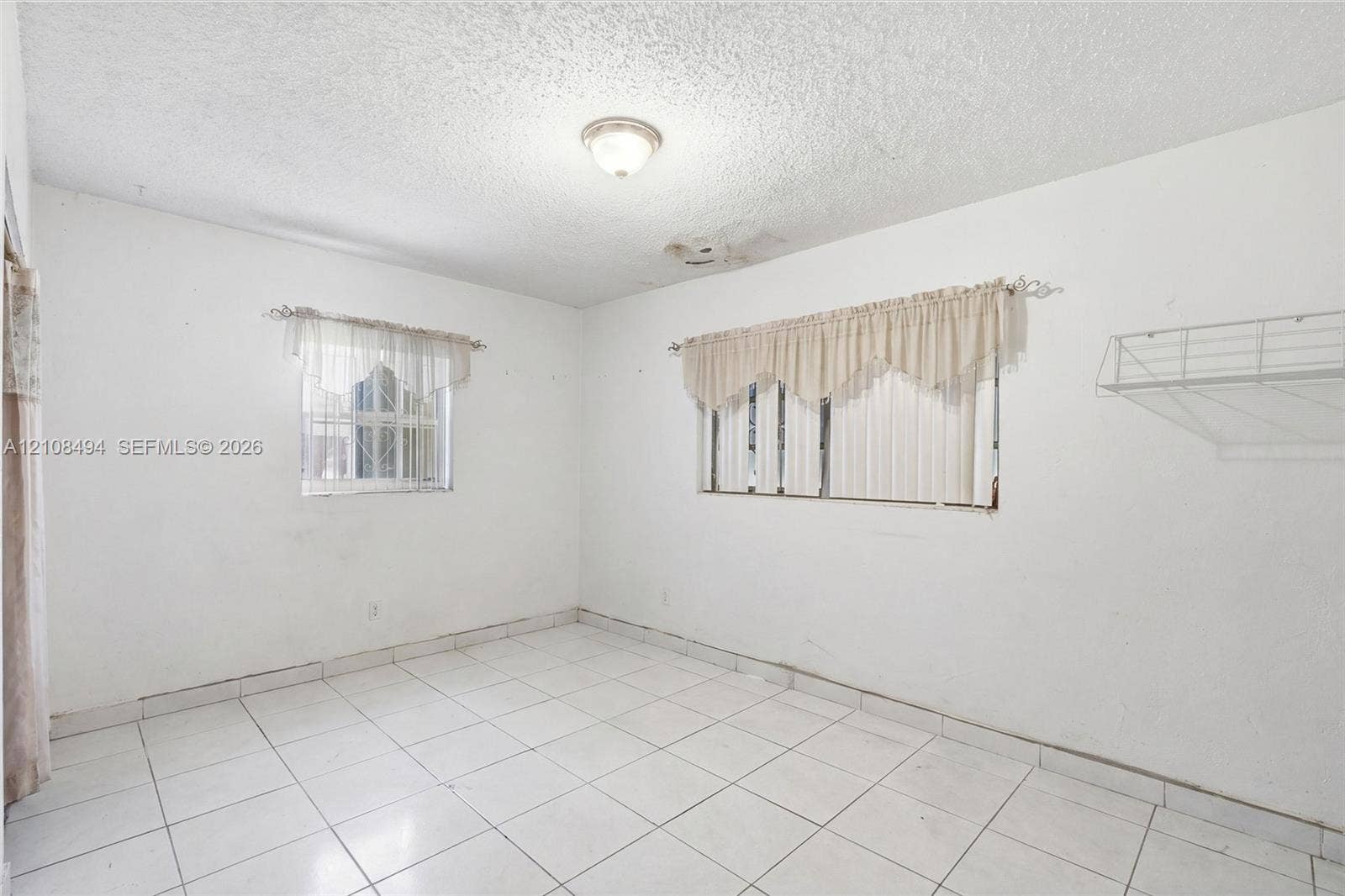6940 NW 28th Avenue, Miami, FL 33147 Interior space featuring white floor tiles, a dual-window configuration, a flush-mount ceiling light fixture, and a built-in wire wall shelf