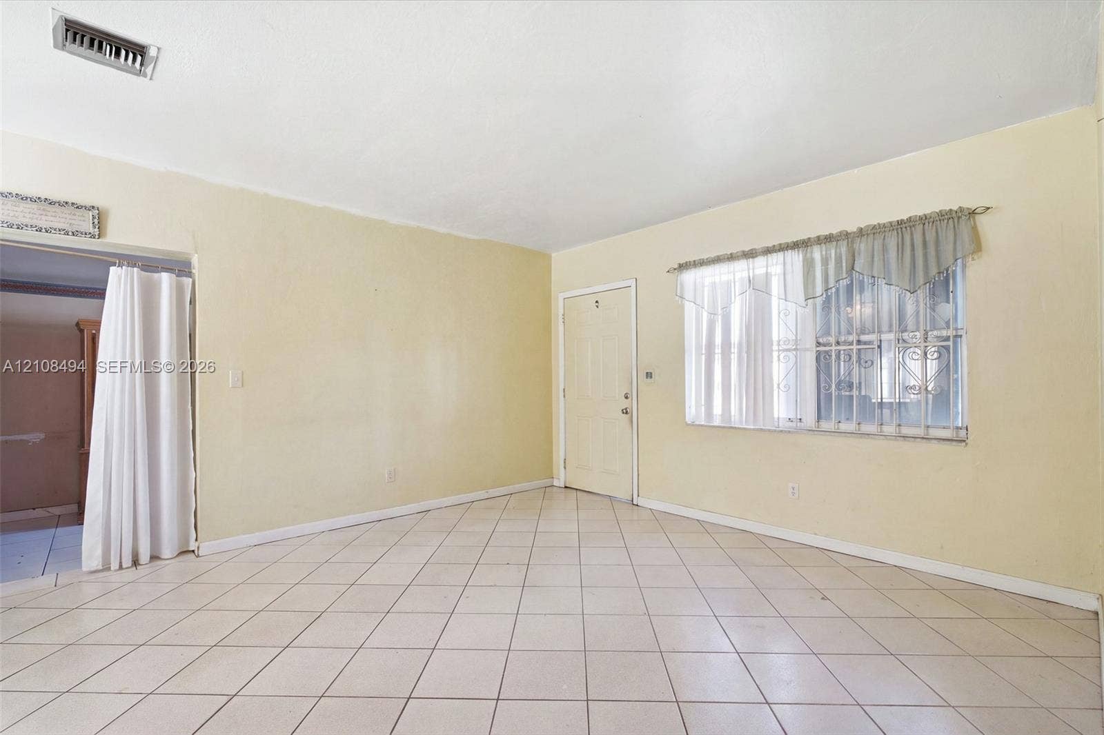 6940 NW 28th Avenue, Miami, FL 33147 Interior space featuring diagonal-patterned ceramic tile flooring, neutral wall paint, and a window equipped with metal security bars