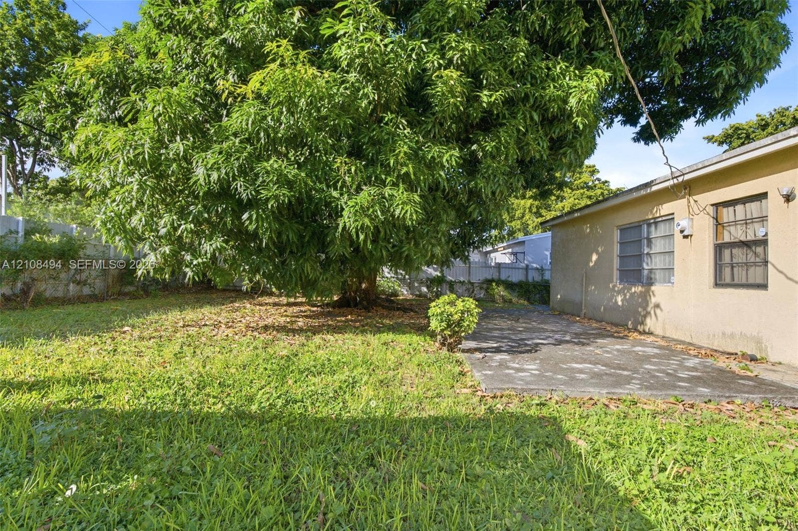 6940 NW 28th Avenue, Miami, FL 33147 Backyard featuring a mature tree, concrete patio, grass lawn, and perimeter fencing