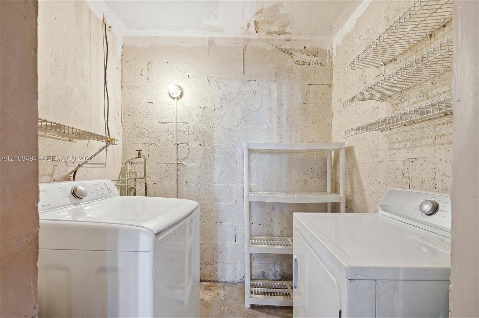 6940 NW 28th Avenue, Miami, FL 33147 Utility area featuring concrete masonry unit walls, wire shelving, and exposed plumbing connections