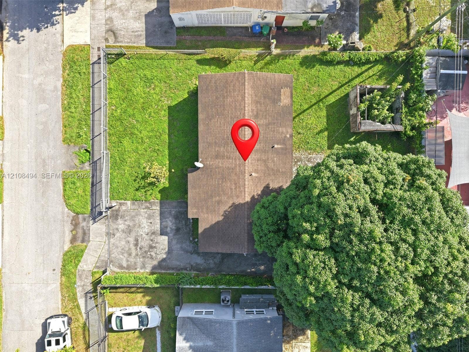 6940 NW 28th Avenue, Miami, FL 33147 Aerial perspective of property lot featuring an expansive lawn, concrete driveway, perimeter chain-link fencing, and mature trees