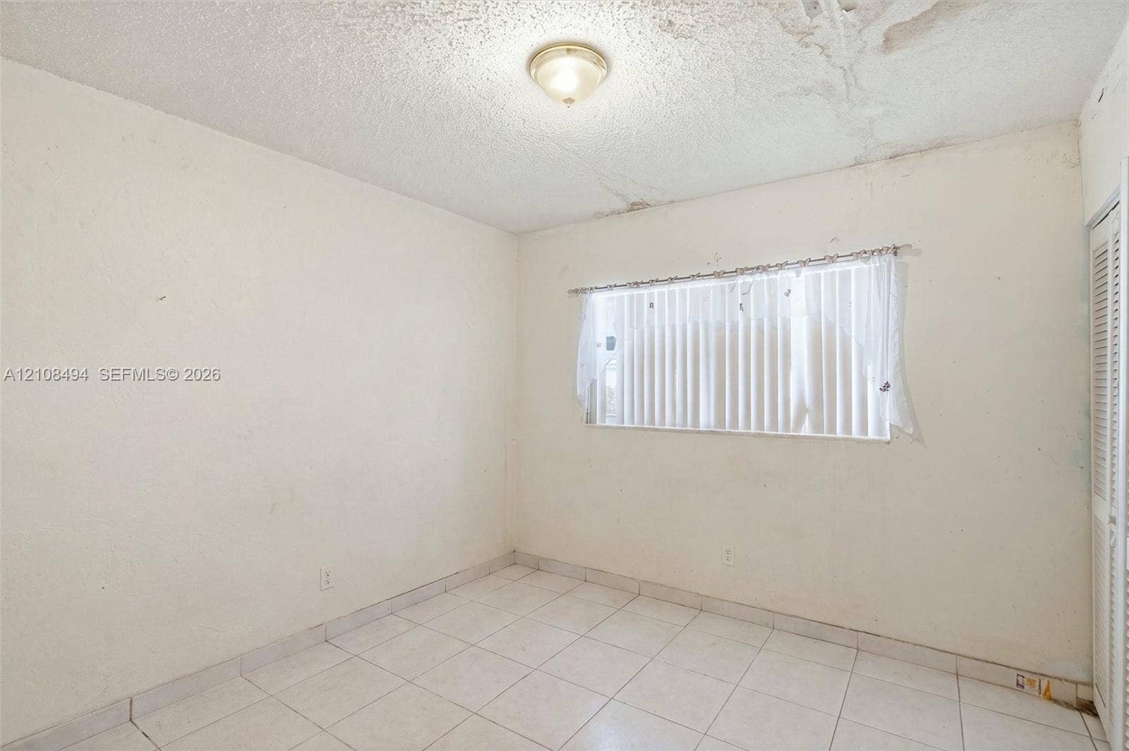 6940 NW 28th Avenue, Miami, FL 33147 Room featuring white tile flooring, ceiling-mounted flush lighting, and a louvered bi-fold closet door