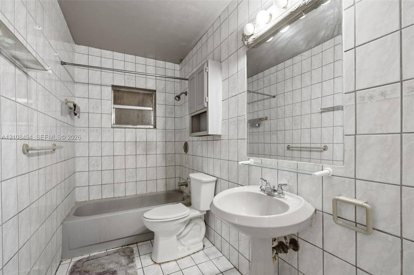 6940 NW 28th Avenue, Miami, FL 33147 Full-height tile wall surround, white pedestal sink, integrated wall-mounted medicine cabinet, wall-to-wall mirror with glass shelving, and porcelain tub with shower head fixture