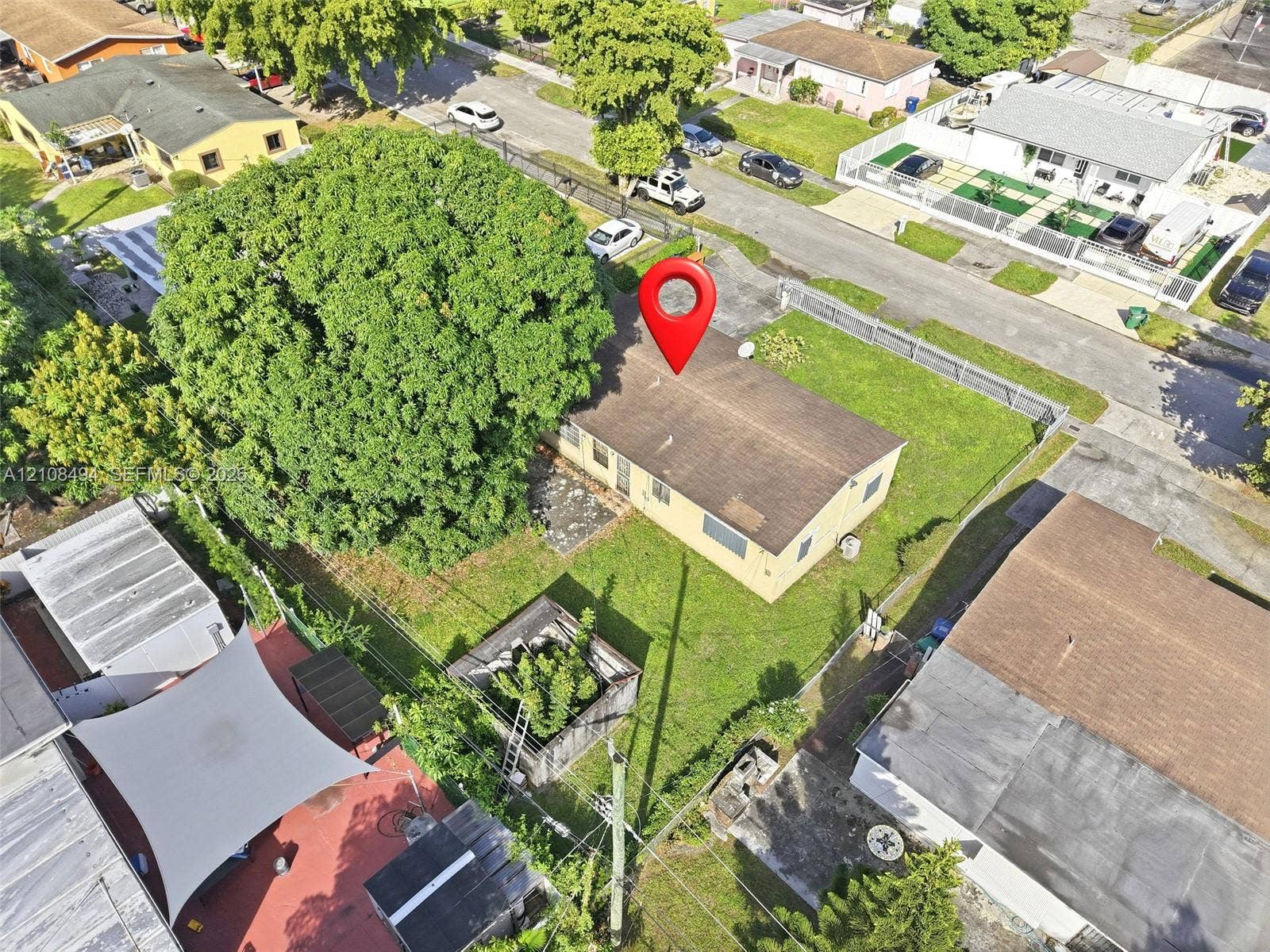6940 NW 28th Avenue, Miami, FL 33147 Aerial perspective of a detached single-story residence featuring a shingled roof, exterior masonry siding, a fenced perimeter, and mature canopy trees on a grass-covered lot