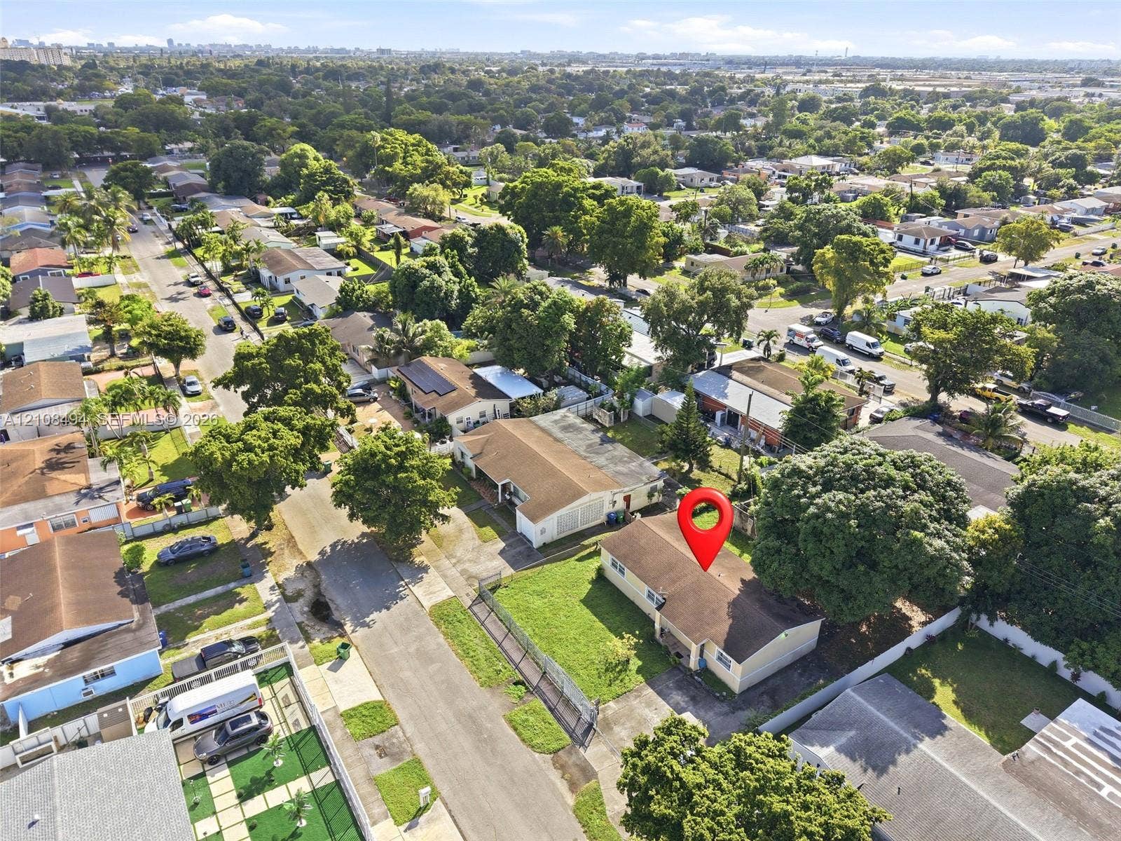 6940 NW 28th Avenue, Miami, FL 33147 Aerial perspective of a single-story residence featuring a shingled roof, a concrete driveway, and established trees within a residential neighborhood