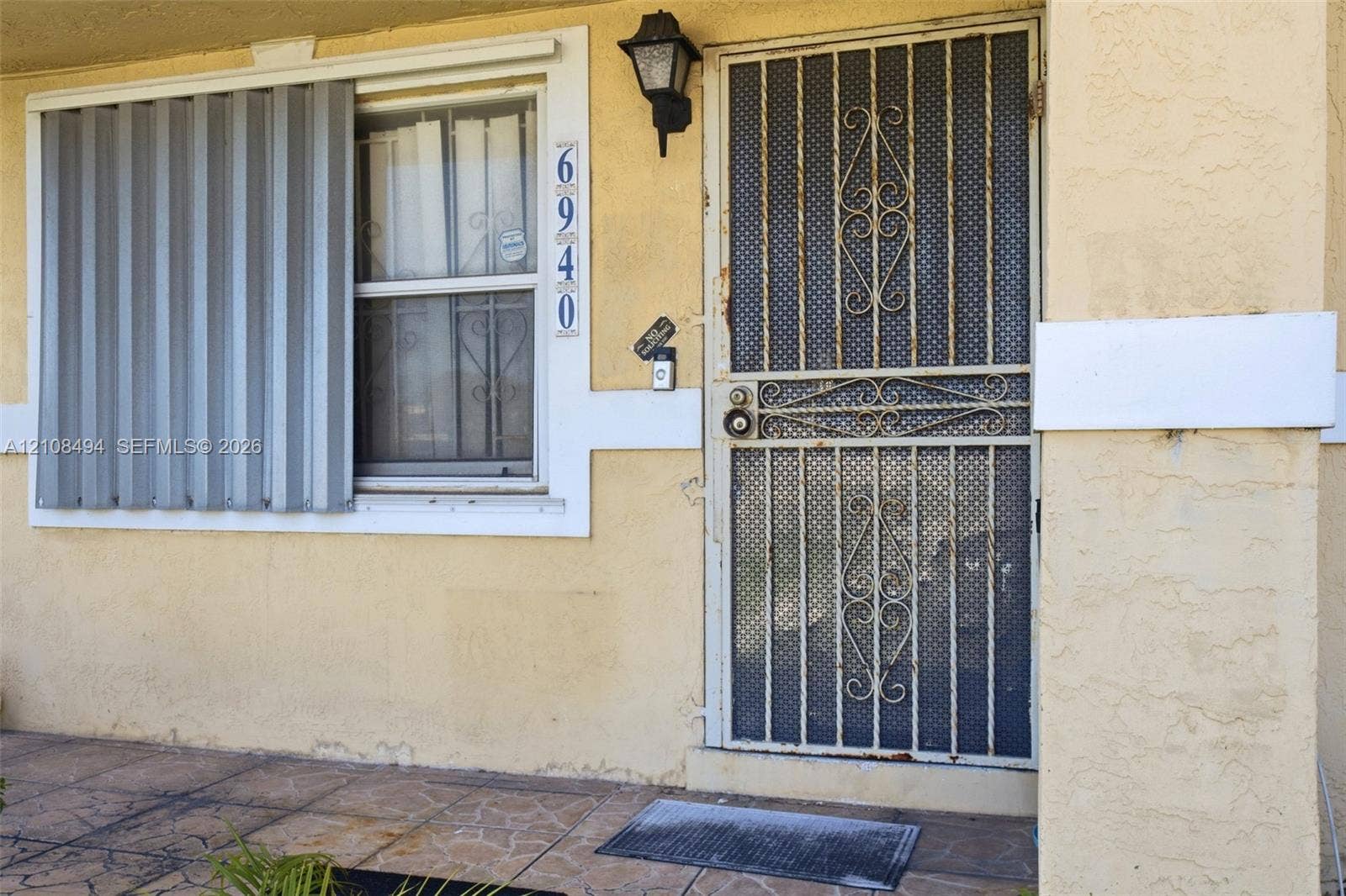 6940 NW 28th Avenue, Miami, FL 33147 Stucco exterior entry featuring a decorative metal screen door, exterior storm shutters, and tiled porch flooring