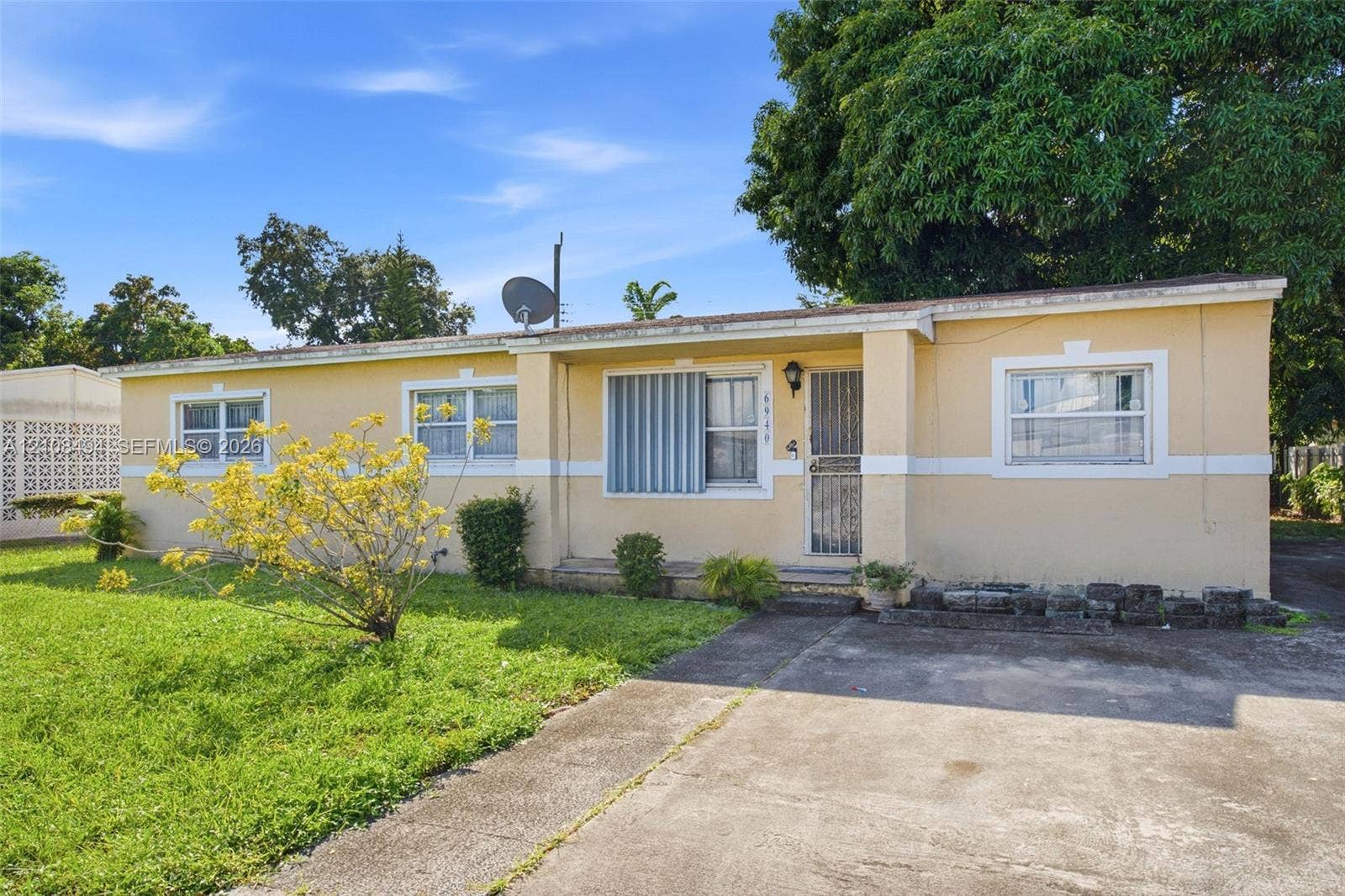 6940 NW 28th Avenue, Miami, FL 33147 Single-story residence featuring a stucco exterior, concrete driveway, metal window shutters, and a covered entryway