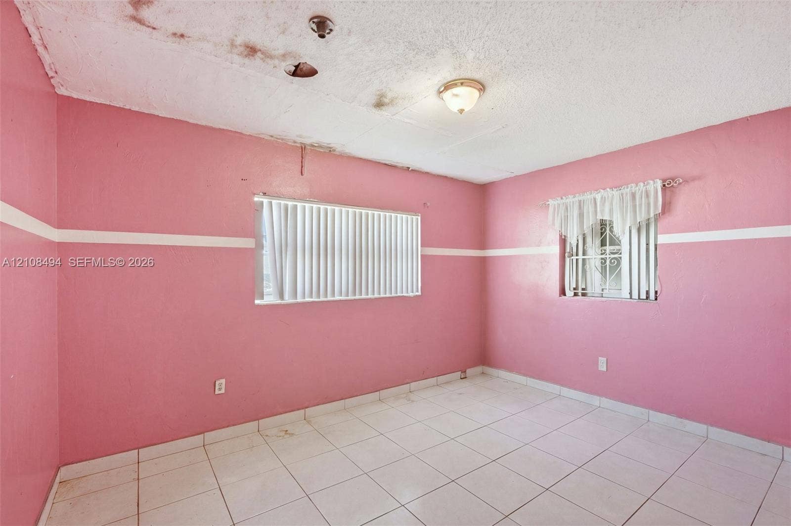 6940 NW 28th Avenue, Miami, FL 33147 Tile flooring throughout featuring two windows with horizontal blinds and an attached ceiling-mounted light fixture