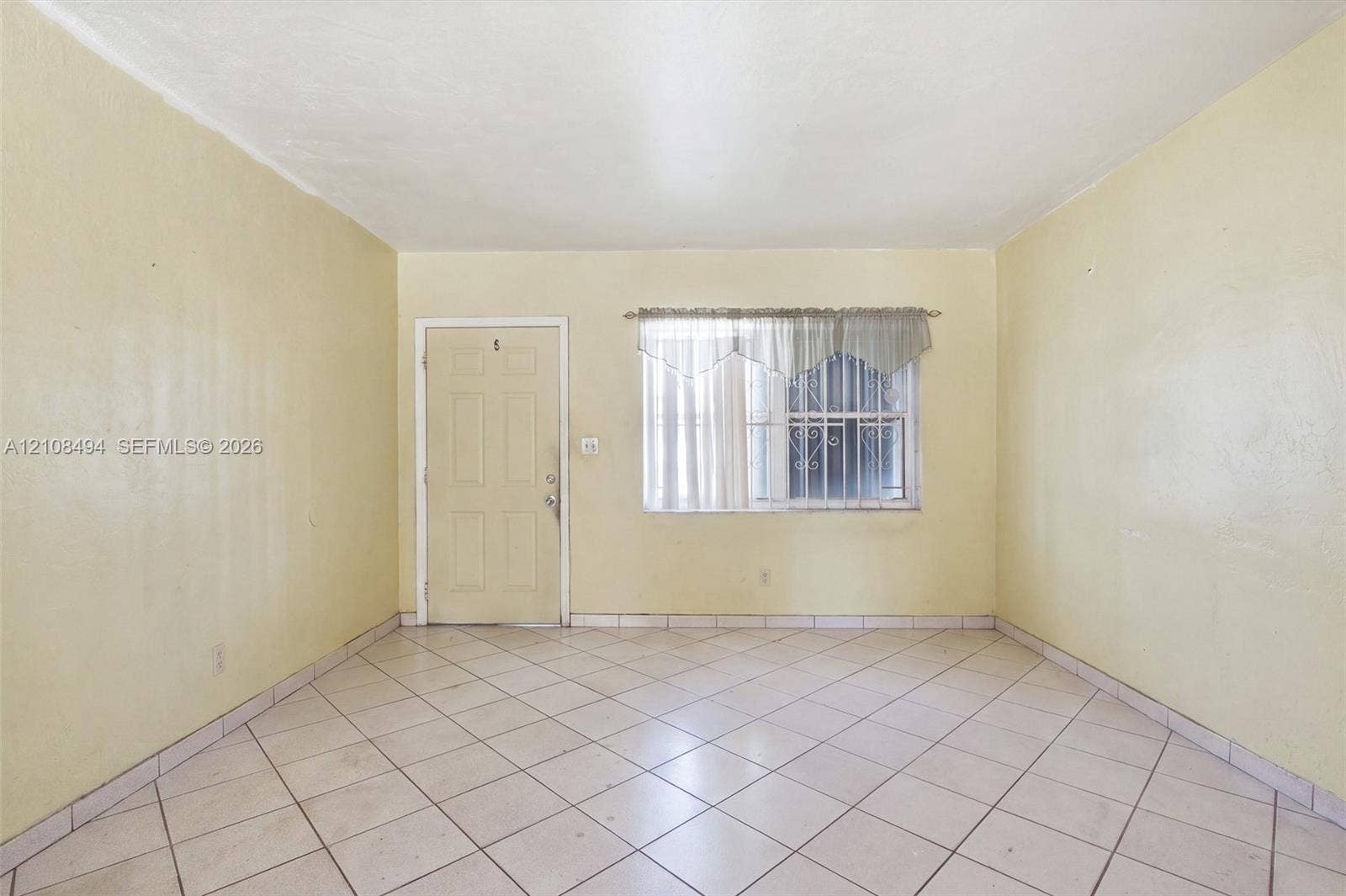 6940 NW 28th Avenue, Miami, FL 33147 Interior space featuring diagonal ceramic tile flooring, a six-panel exterior entry door, and a window with security bars