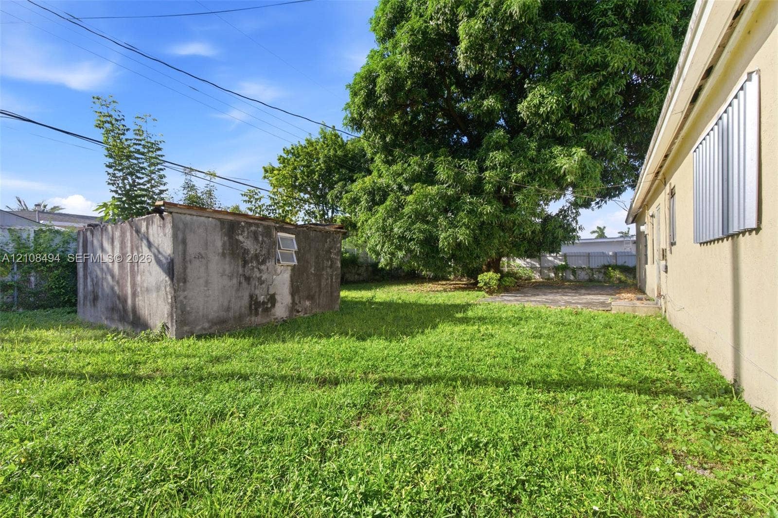 6940 NW 28th Avenue, Miami, FL 33147 Rear yard featuring a grass lawn, mature tree, masonry outbuilding, and concrete patio area