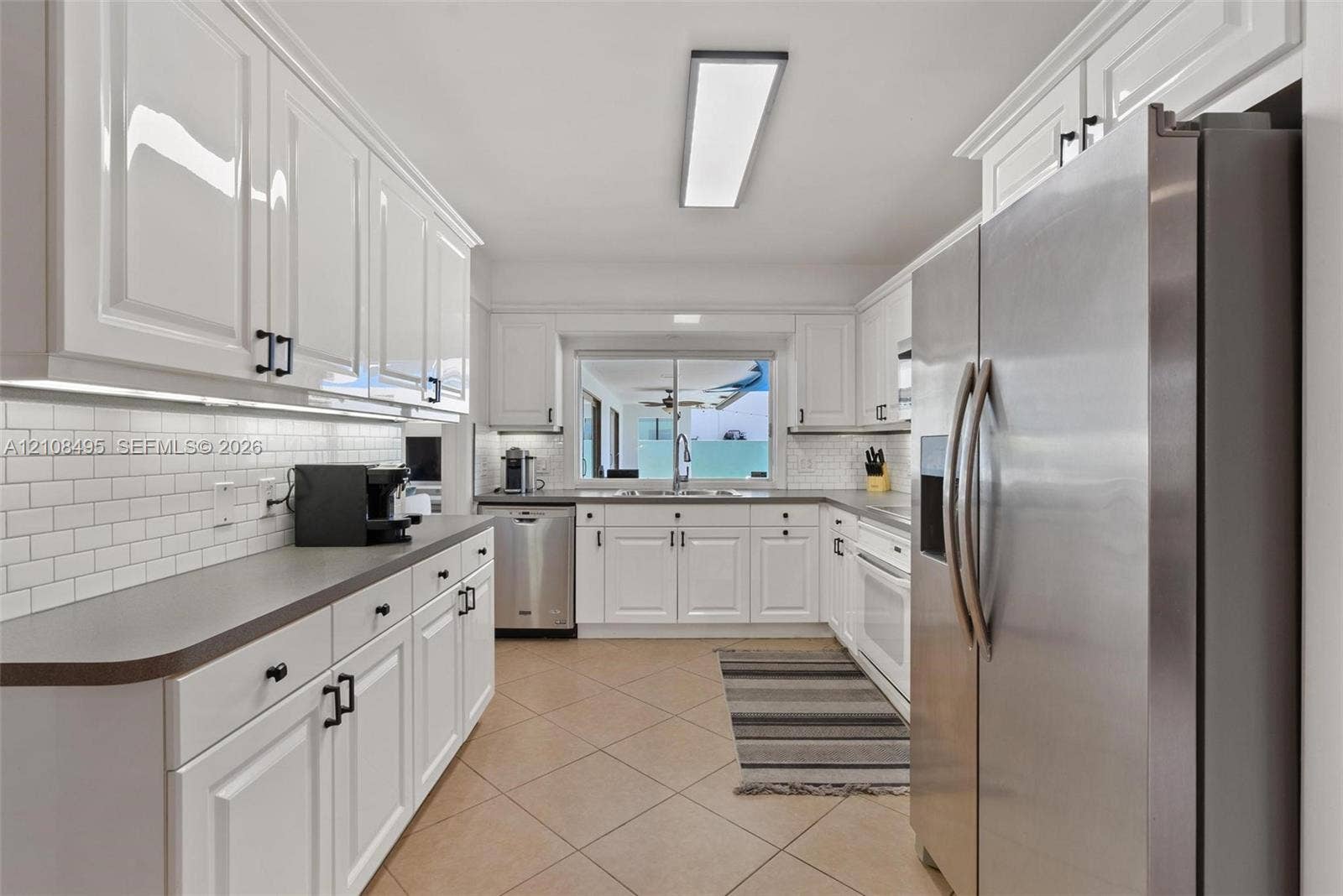 3080 NE 43rd Street, Fort Lauderdale, FL 33308 Kitchen featuring white shaker-style cabinetry, matte black hardware, white subway tile backsplash, solid-surface countertops, and stainless steel appliances