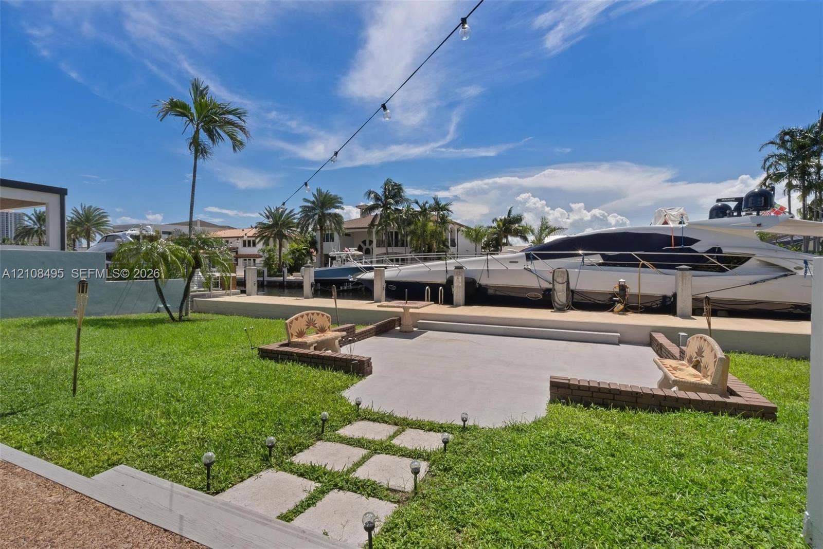 3080 NE 43rd Street, Fort Lauderdale, FL 33308 Waterfront backyard featuring a concrete patio, stone-surfaced retaining walls, manicured lawn, and a private bulkhead boat dock