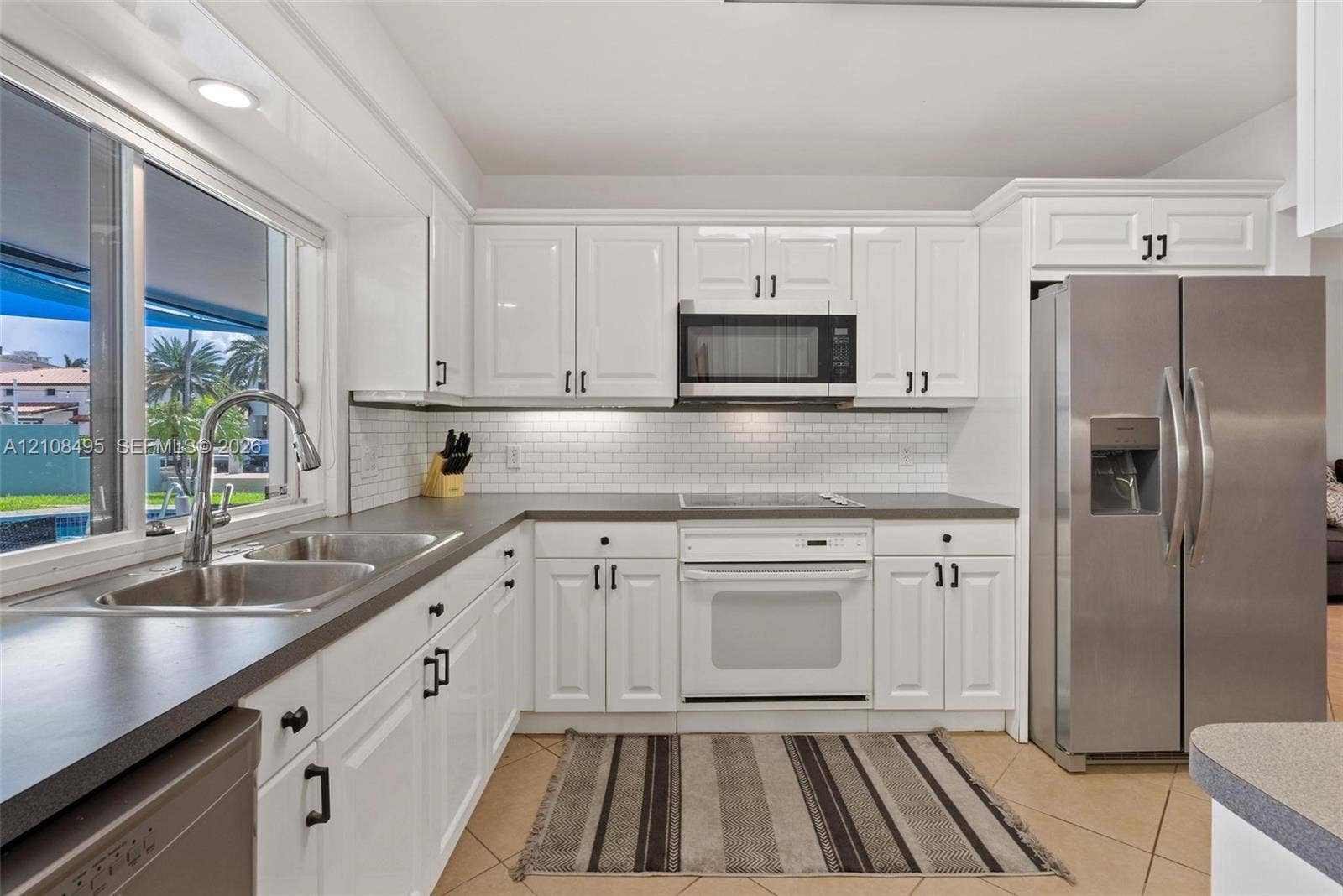 3080 NE 43rd Street, Fort Lauderdale, FL 33308 Kitchen featuring white cabinetry, subway tile backsplash, dark solid-surface countertops, stainless steel side-by-side refrigerator, and double-basin sink with pull-down faucet