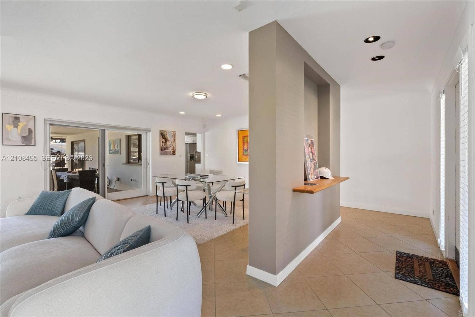 3080 NE 43rd Street, Fort Lauderdale, FL 33308 Open-concept living space featuring large-format diagonal tile flooring, a central partition wall with a recessed display niche and built-in wood shelf, recessed ceiling lighting, and sliding glass doors