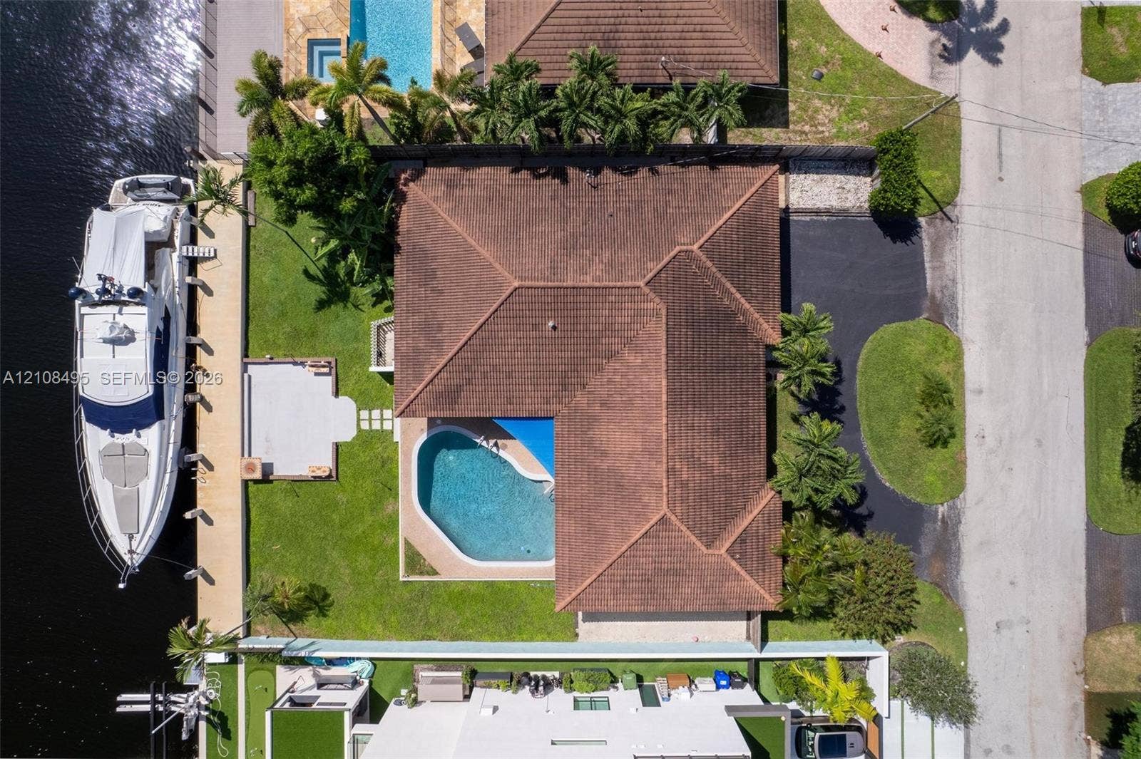 3080 NE 43rd Street, Fort Lauderdale, FL 33308 Aerial view of a waterfront property featuring a private boat dock, a swimming pool, a tiled roof, and a paved driveway