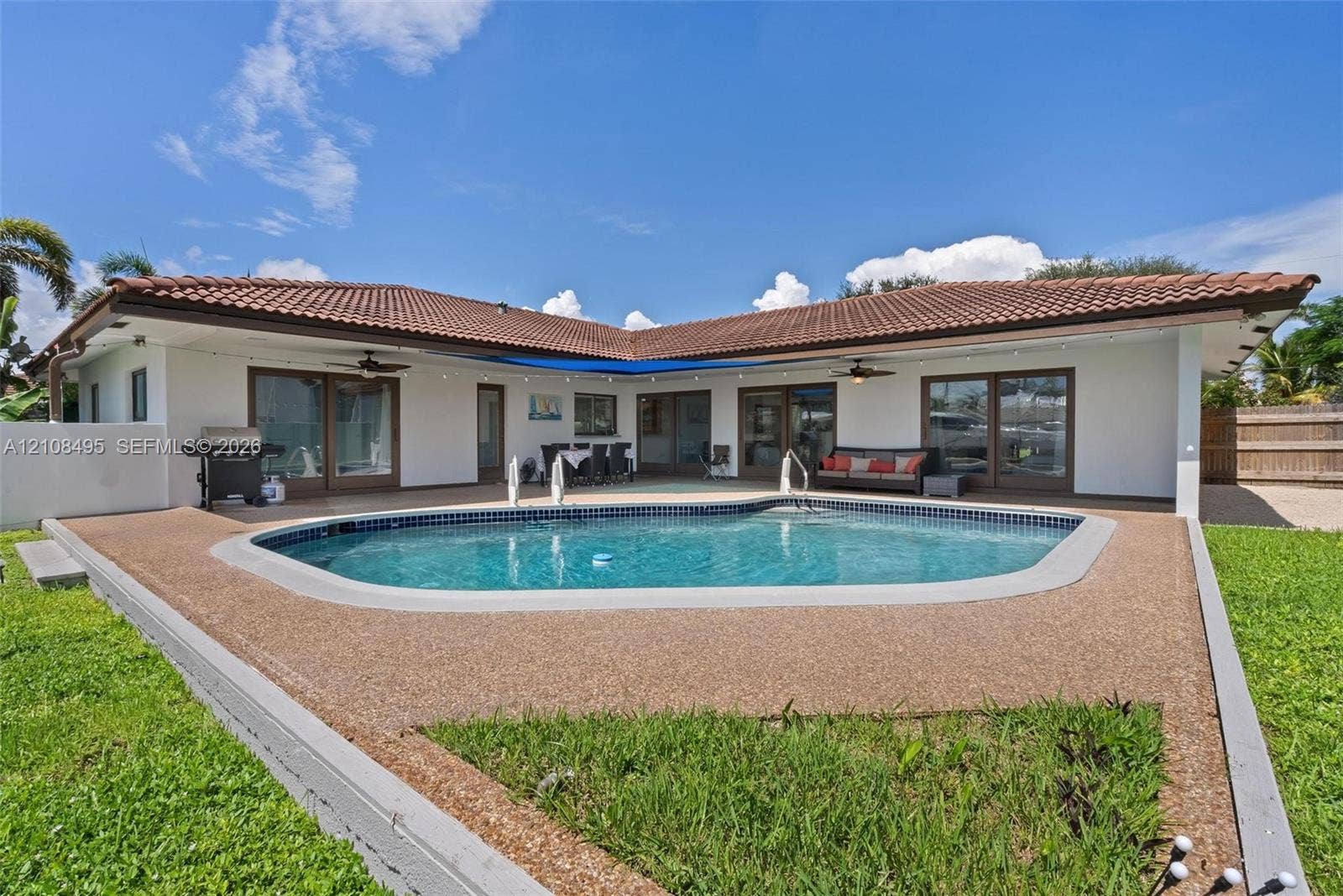 3080 NE 43rd Street, Fort Lauderdale, FL 33308 L-shaped exterior featuring a tiled roof, in-ground swimming pool with aggregate decking, and multiple sliding glass door entries