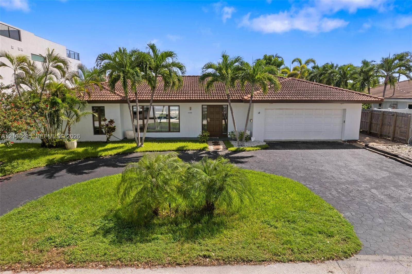3080 NE 43rd Street, Fort Lauderdale, FL 33308 Single-story exterior featuring white stucco siding, a tiled roof, a multi-car garage, and a paved circular driveway