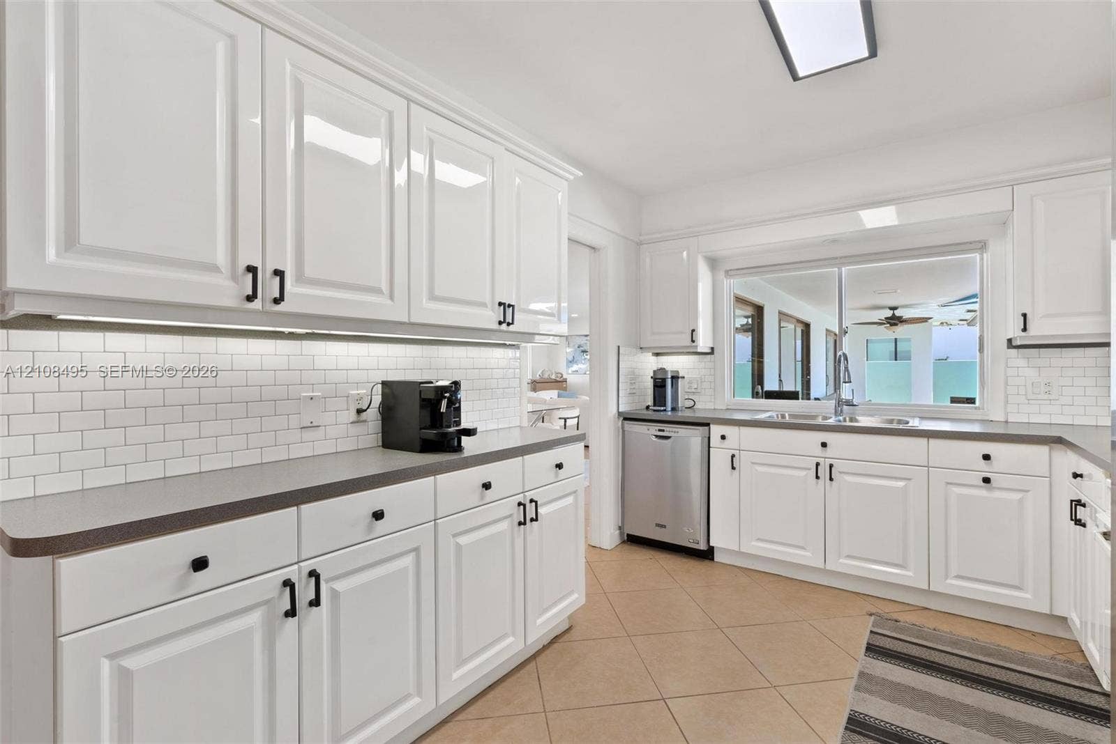 3080 NE 43rd Street, Fort Lauderdale, FL 33308 Kitchen featuring white cabinetry, subway tile backsplash, solid-surface countertops, stainless steel dishwasher, and tile flooring