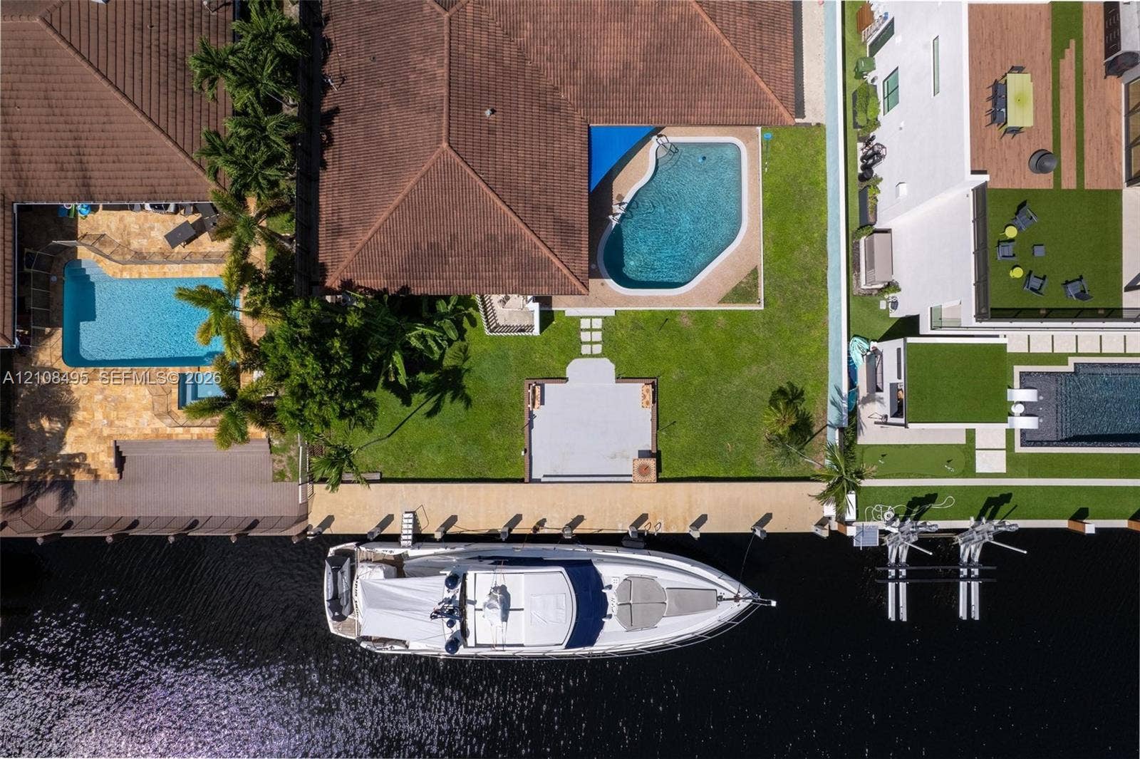3080 NE 43rd Street, Fort Lauderdale, FL 33308 Waterfront property featuring a private concrete dock, an in-ground swimming pool, a sodded lawn, and a paved patio area